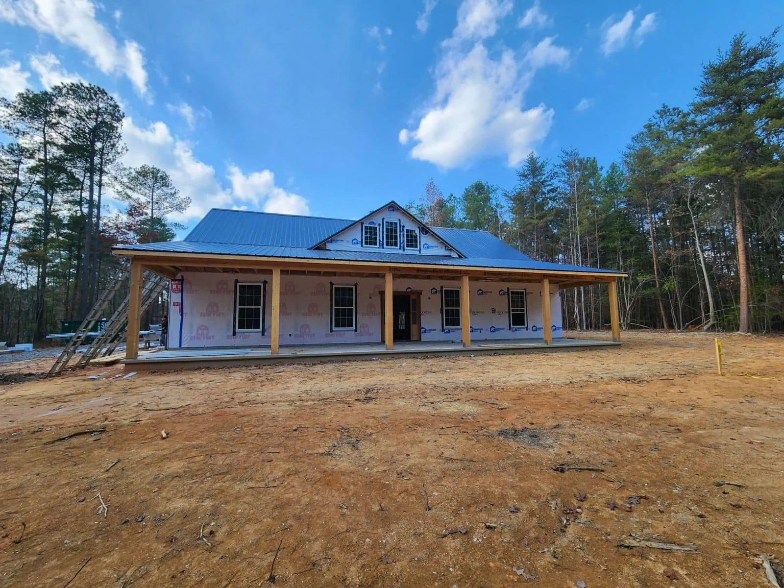 A house under construction with a metal roof, surrounded by trees and a clear blue sky.