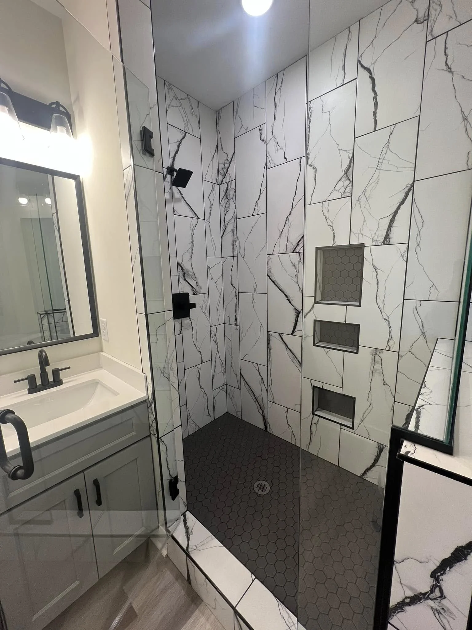 Modern bathroom with a glass shower enclosure, black fixtures, and marble tiles on the walls, with built-in shelves inside the shower.