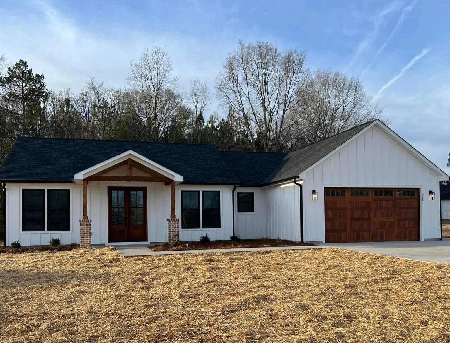 Front view of a modern house with white siding, black roof, and wooden accents, featuring a gabled porch and attached garage.