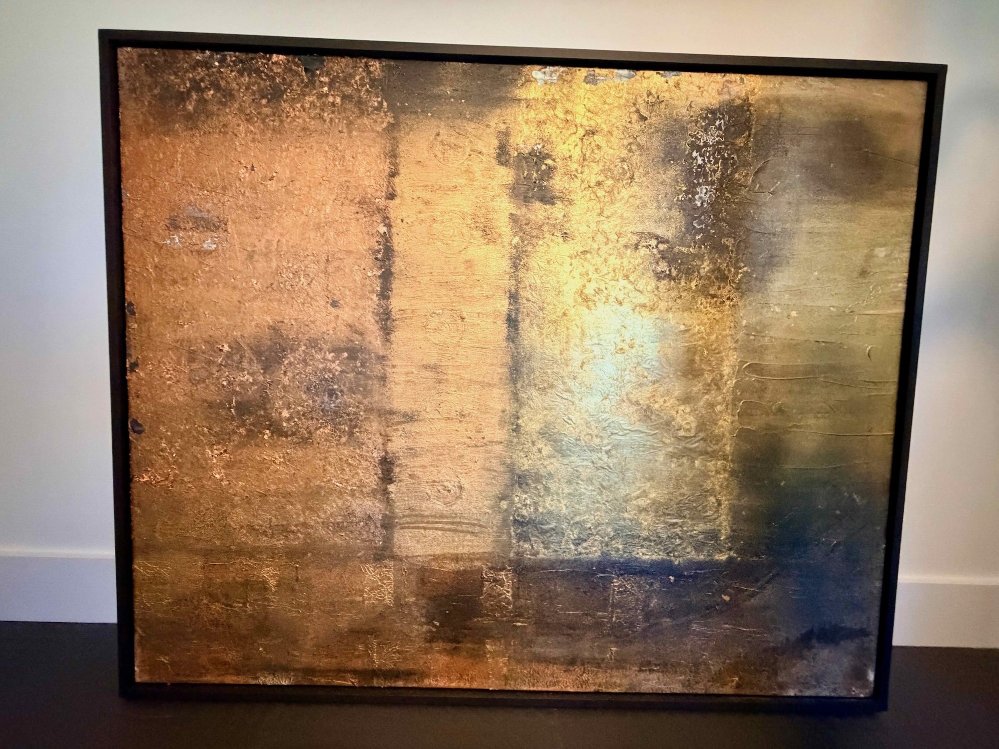 Abstract textured gold and bronze artwork with metallic surface within a black frame.