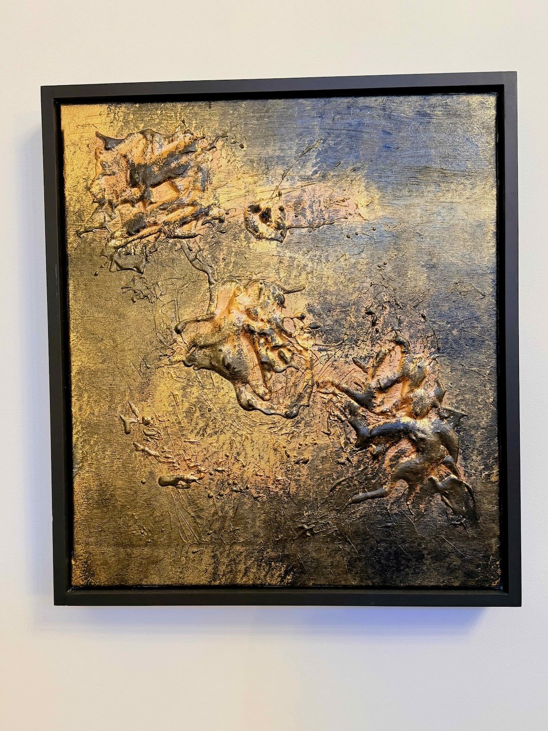 Abstract textured artwork with a metallic finish in shades of gold, bronze, and dark gray, framed in black.