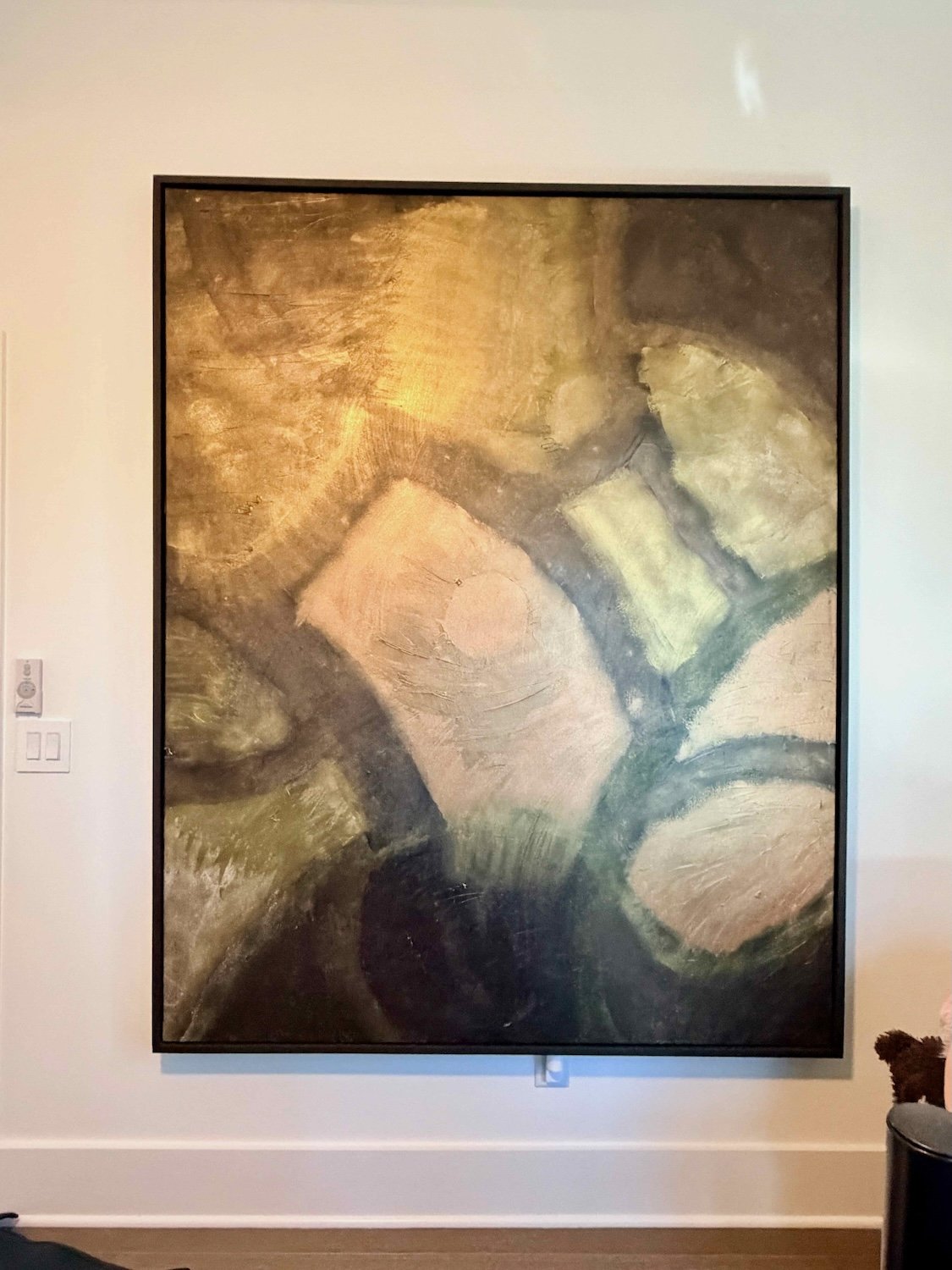 Abstract painting featuring geometric shapes in various muted earth tones on a framed canvas hung on a white gallery wall.