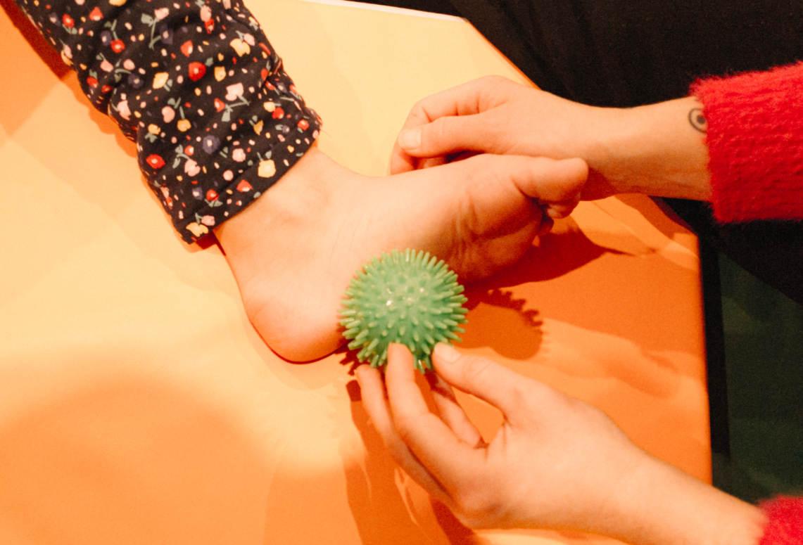 Une personne utilise une balle en caoutchouc spiky pour faire exercer la main et le poignet d'une autre personne, probablement dans un contexte de rééducation ou de thérapie.