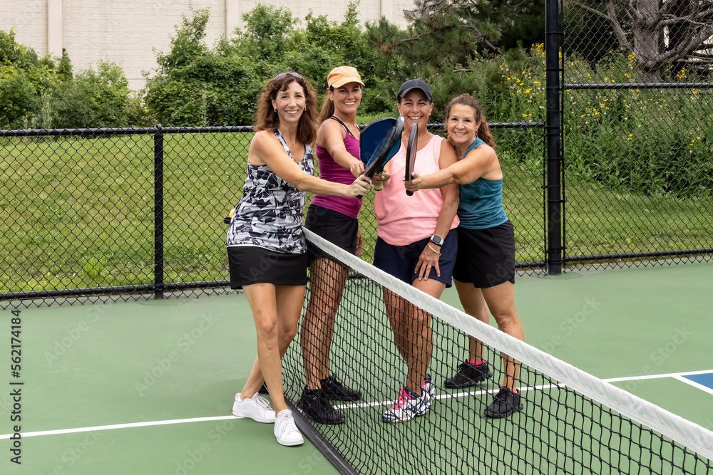 Four women on a pickleball court holding pickleball rackets together, smiling.