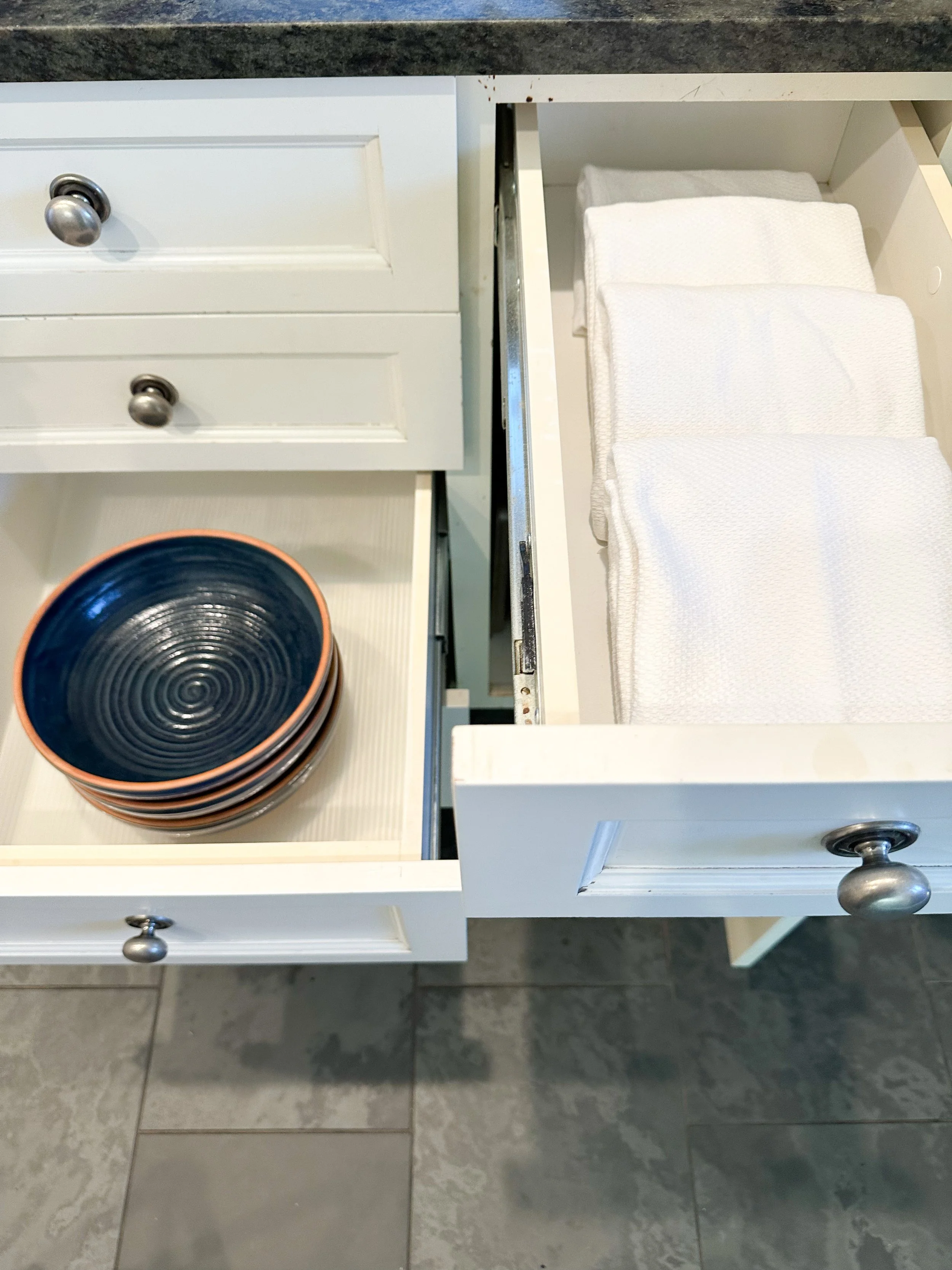 Open kitchen drawer with white cloth napkins and a bowl holding smaller bowls with a dark interior.