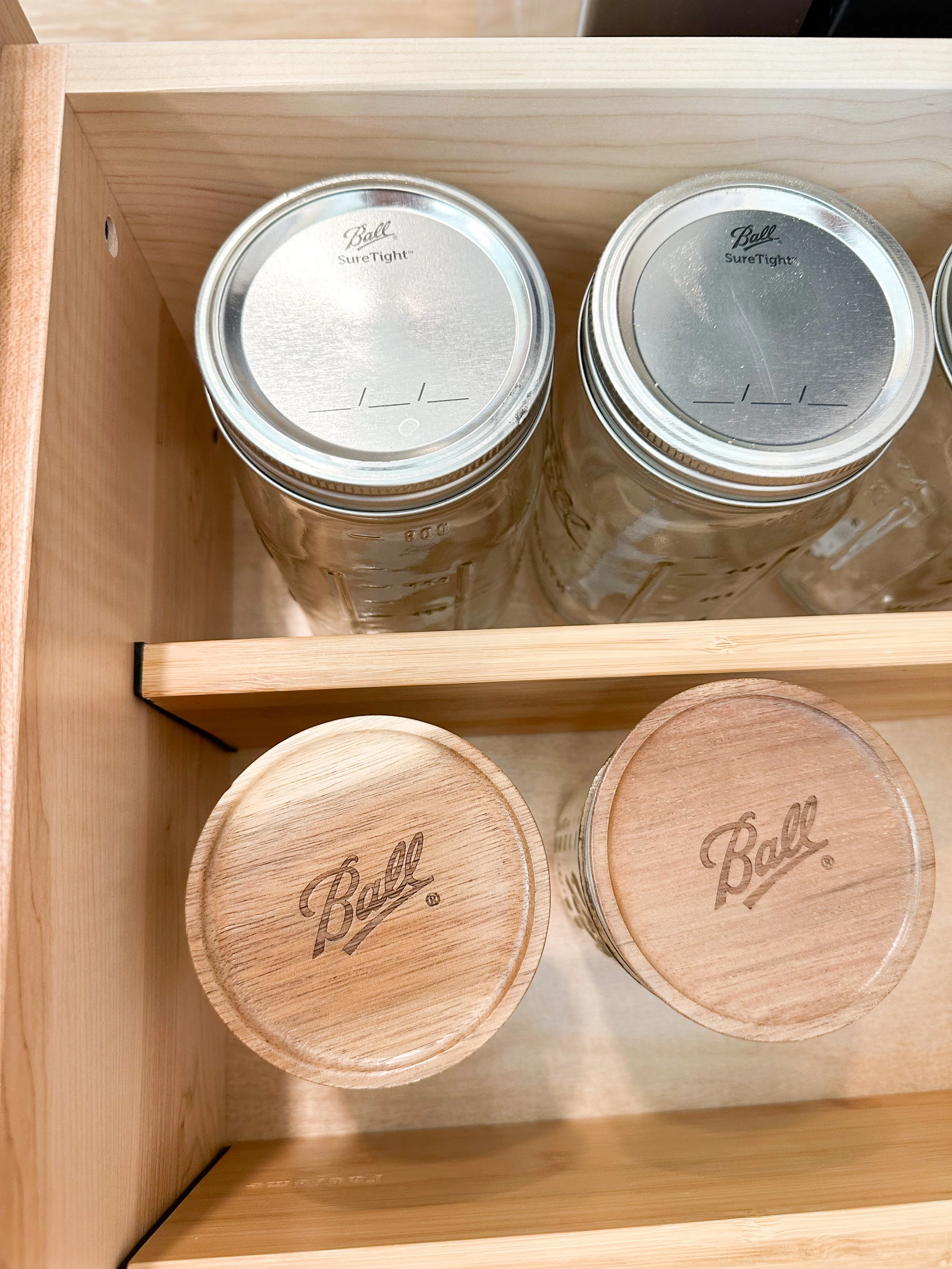 Kitchen drawer with two glass jars with wooden lids labeled 'Ball' and two empty glass jars with metal lids labeled 'Ball'.