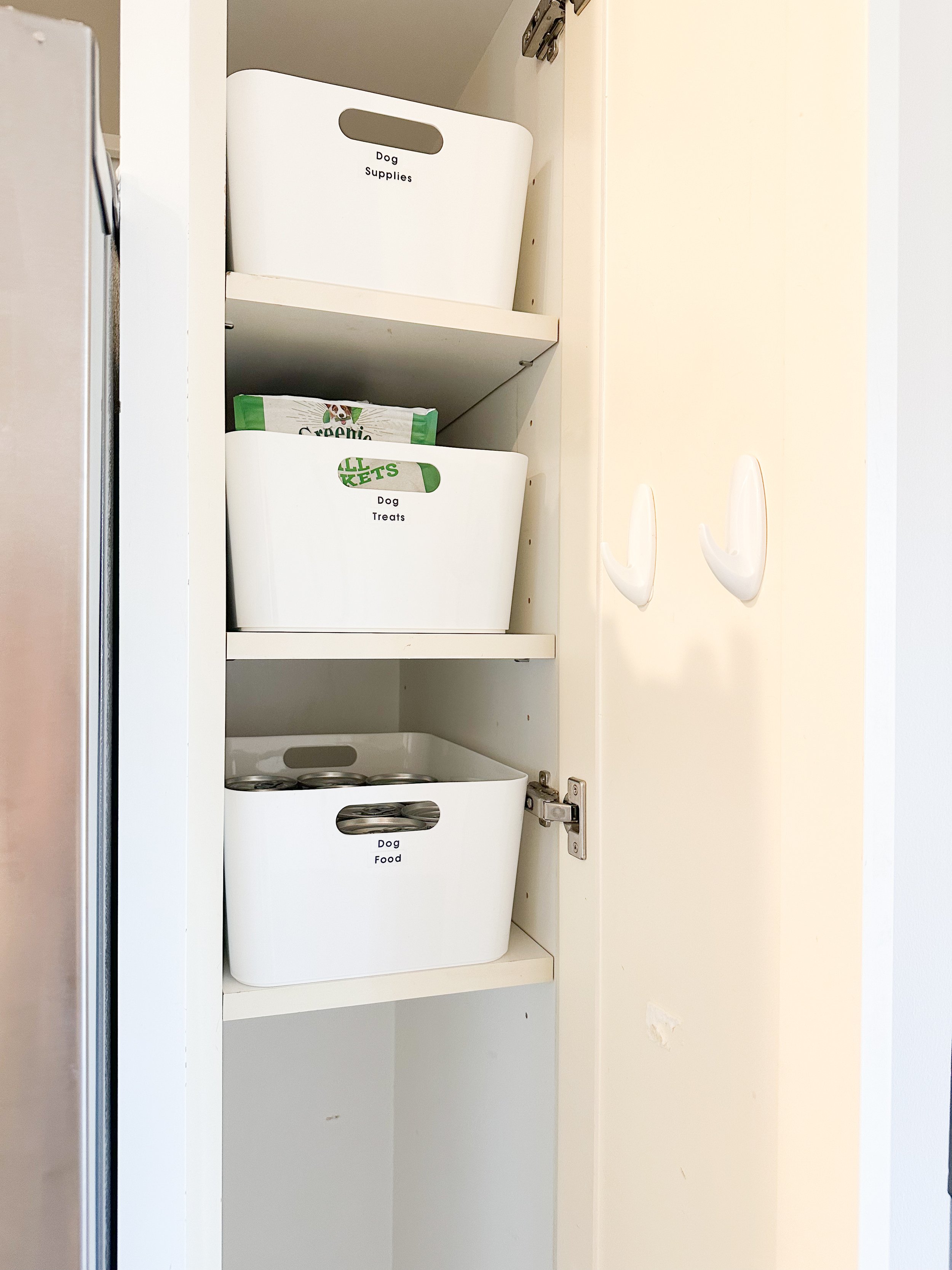 White cabinet shelves containing labeled white containers for dog supplies, treats, and food.