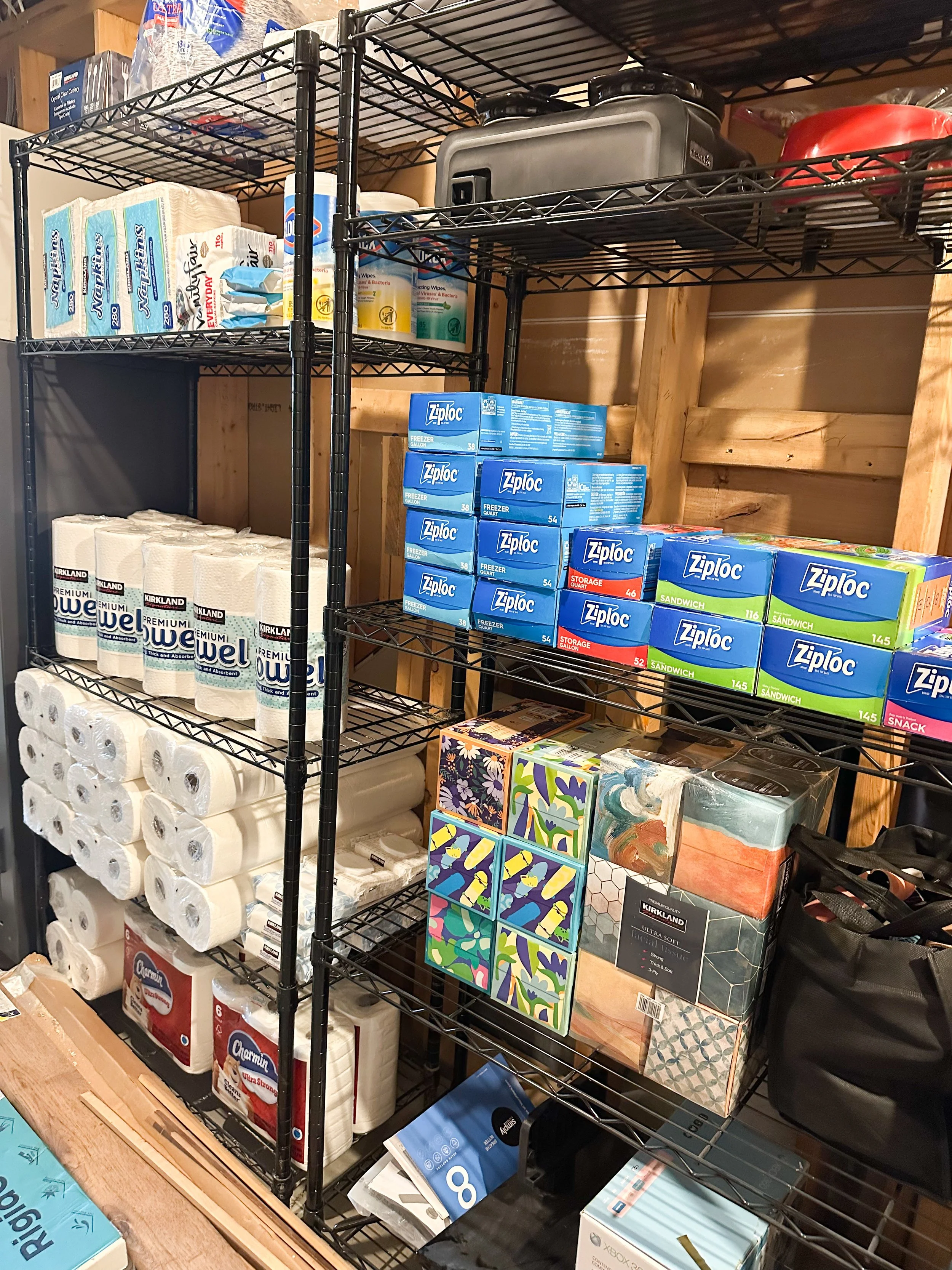 Shelving unit with paper towels, toilet paper, Ziploc bags, tissues, and other household supplies in a storage room.