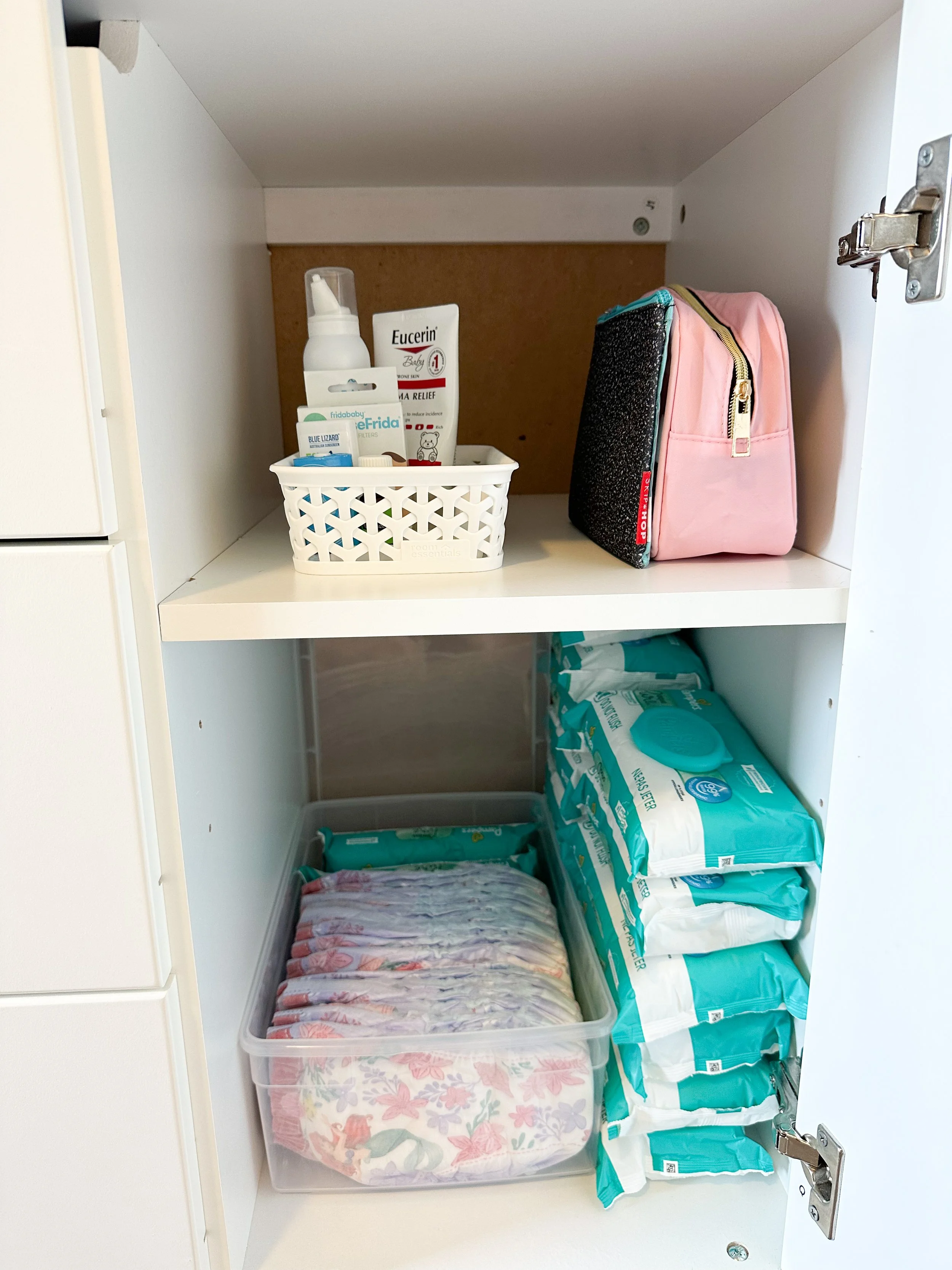 Inside a medicine cabinet with children's diapers, baby wipes, diaper rash cream, hand sanitizer, and a pink bag.