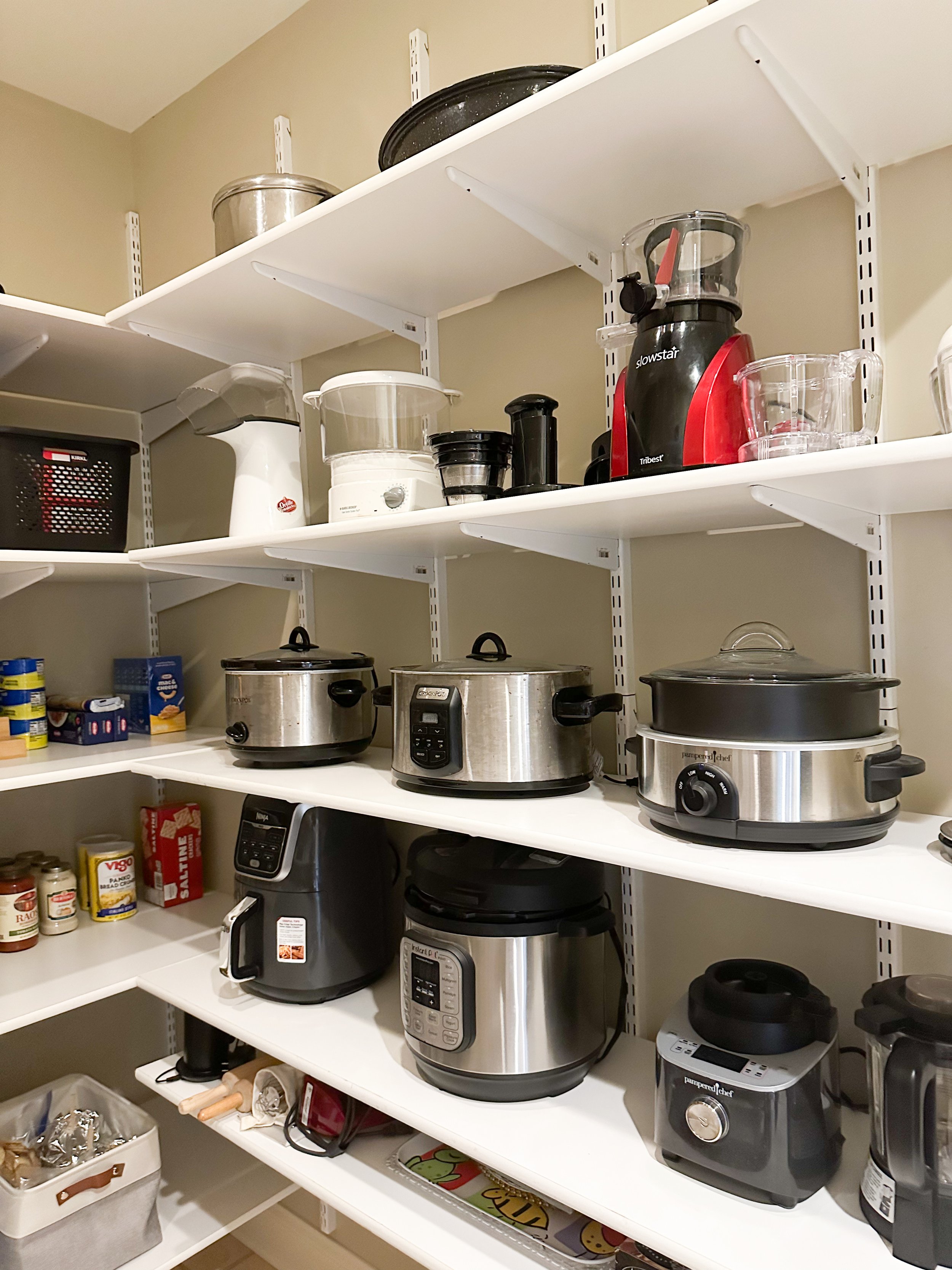 Kitchen pantry with shelves containing various kitchen appliances including rice cookers, slow cookers, blenders, and food storage containers.