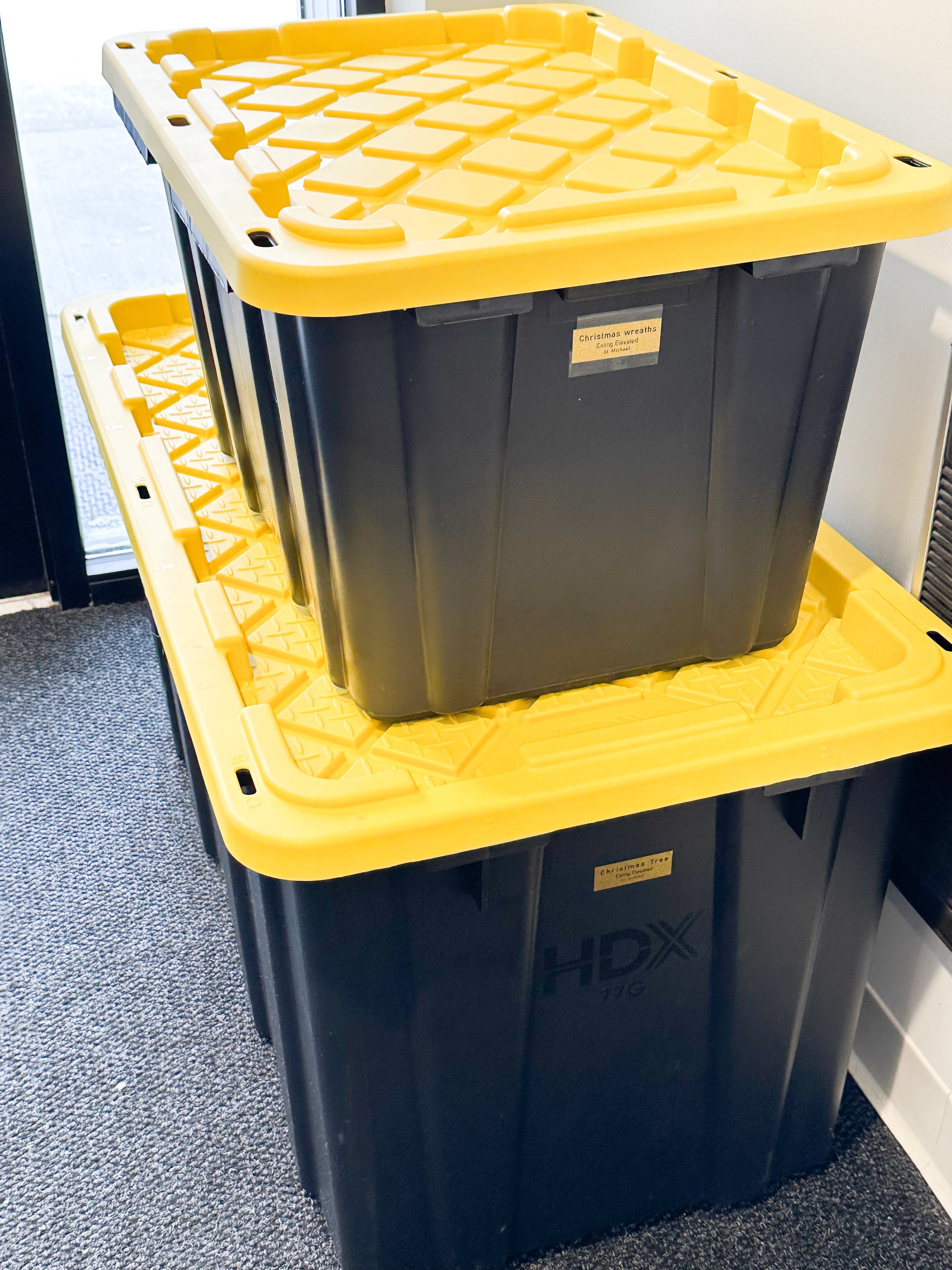 Two large black and yellow storage containers stacked on top of each other, labeled for Christmas wreaths and Christmas trees.