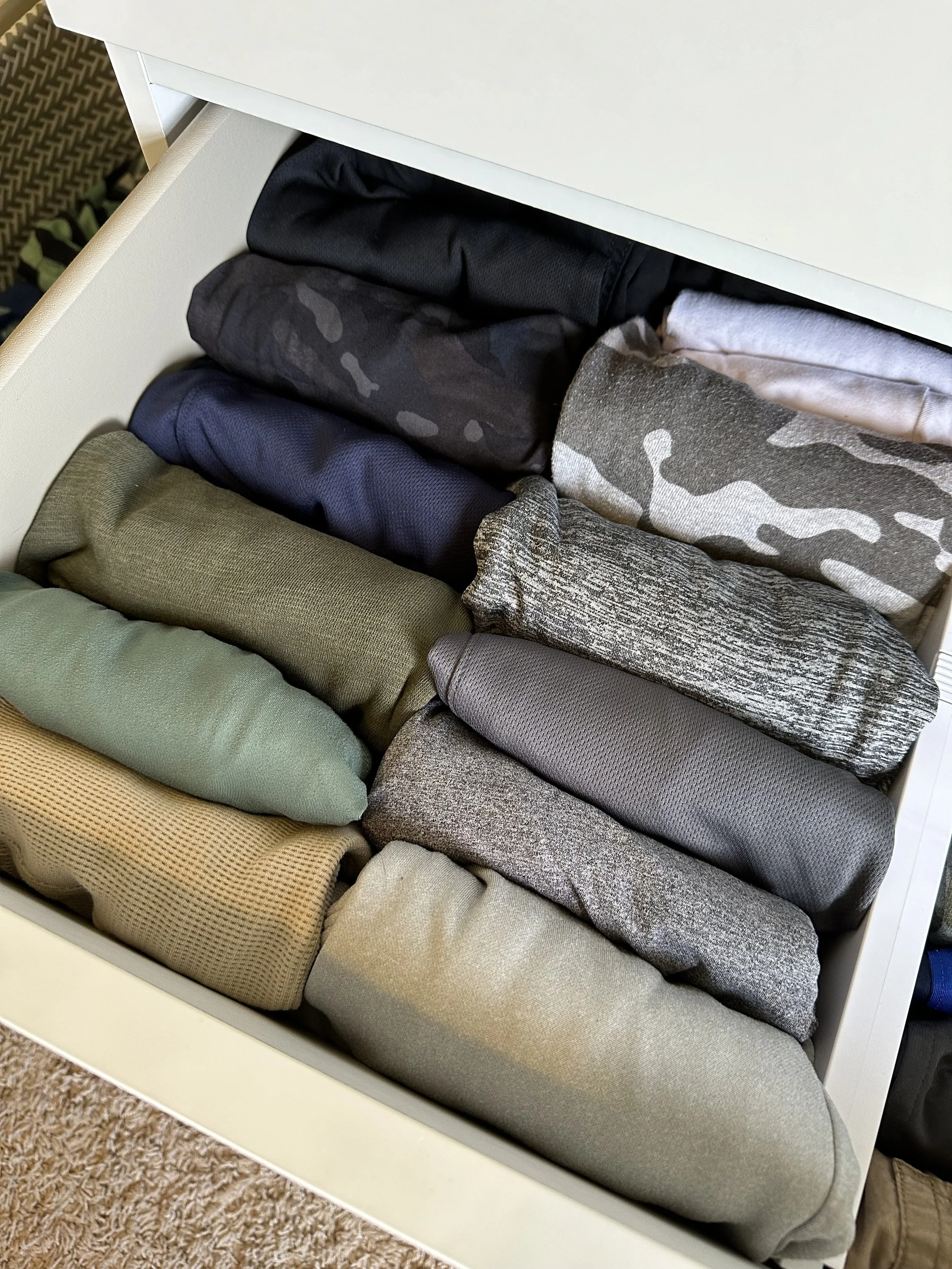 Drawer containing neatly folded men's underwear with various colors and patterns, including black, camouflage, navy, olive green, grey, beige, and textured fabrics.