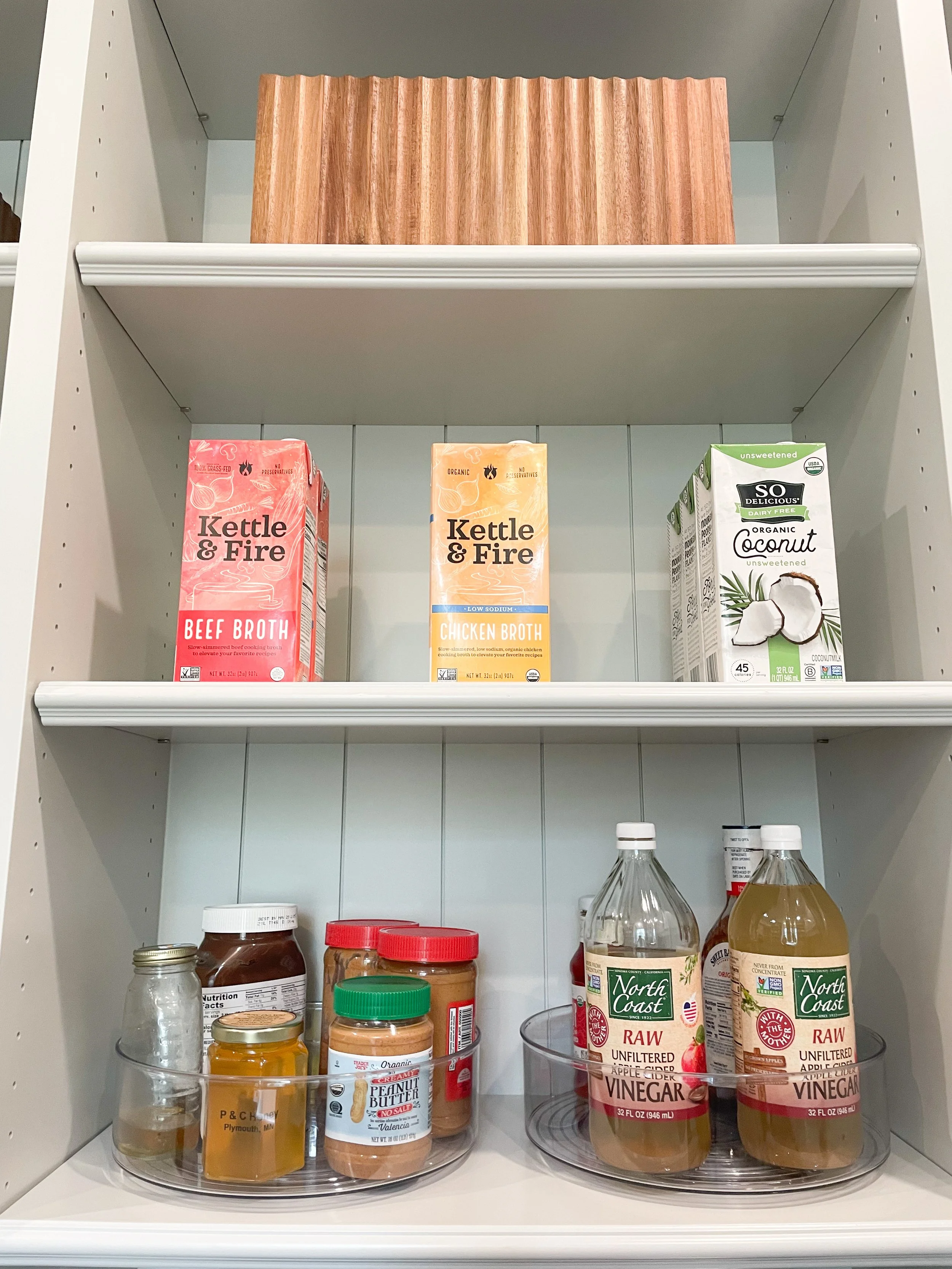Shelves with three cartons of broth, various jars of condiments, and bottles of apple cider vinegar.