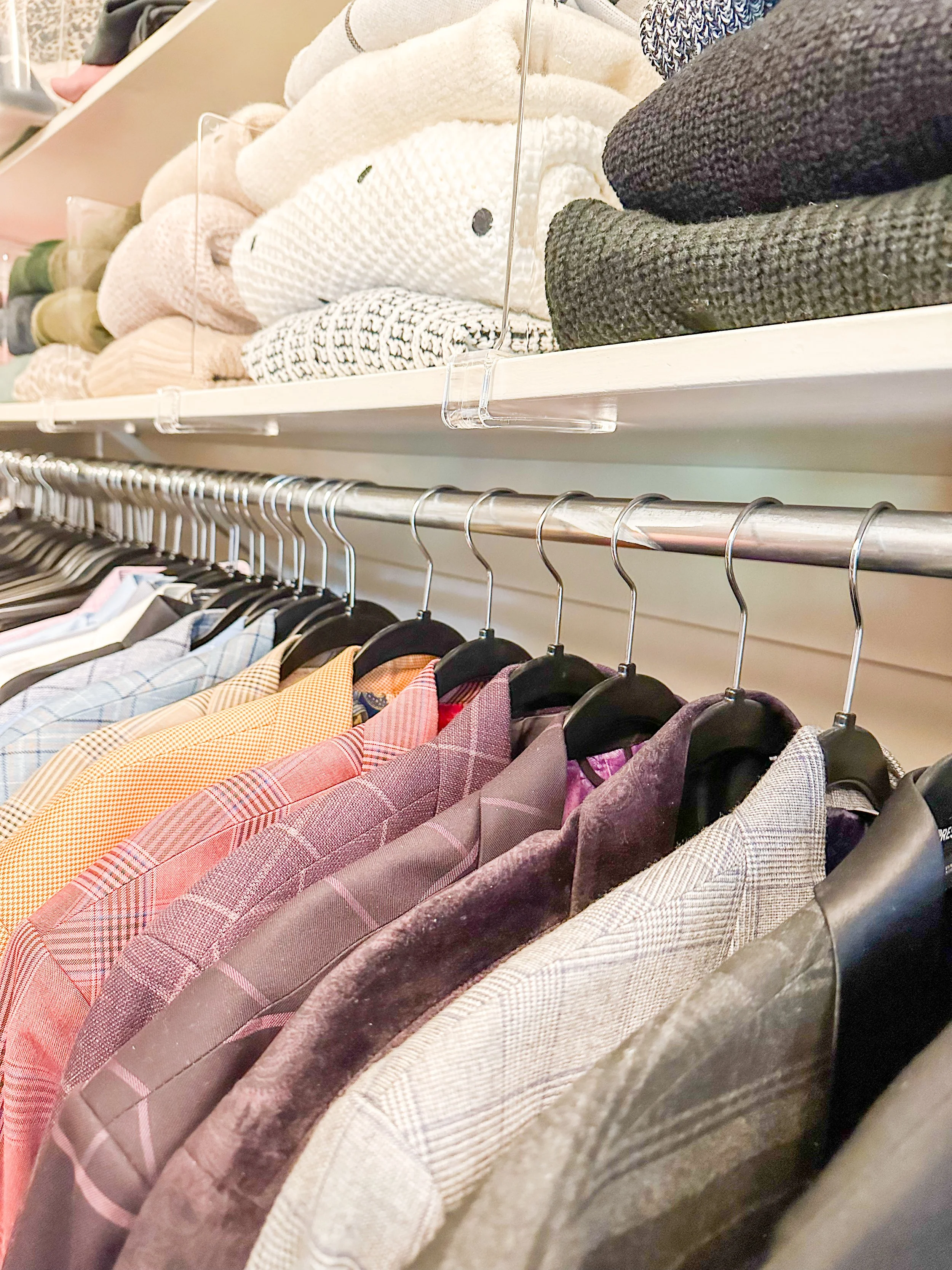 Clothing store shelf displaying folded sweaters on upper shelf and colorful blazers hanging on the lower rack.