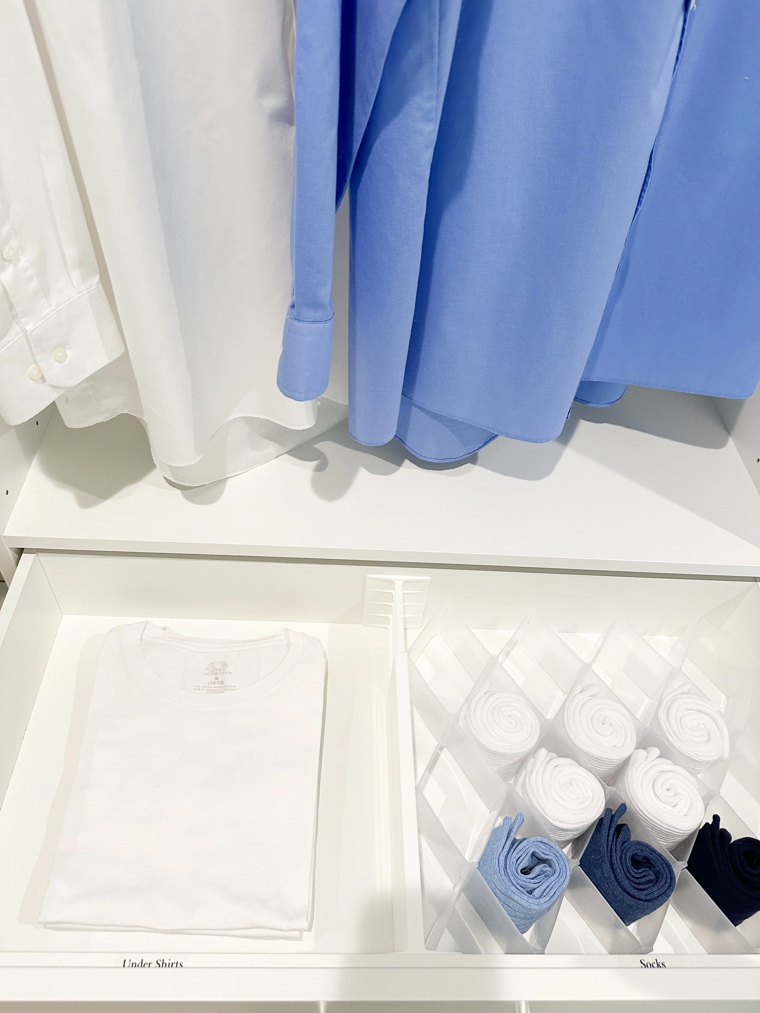 Display of neatly folded white and blue shirts, with white, light blue, and navy socks, on a white table in a clothing store.