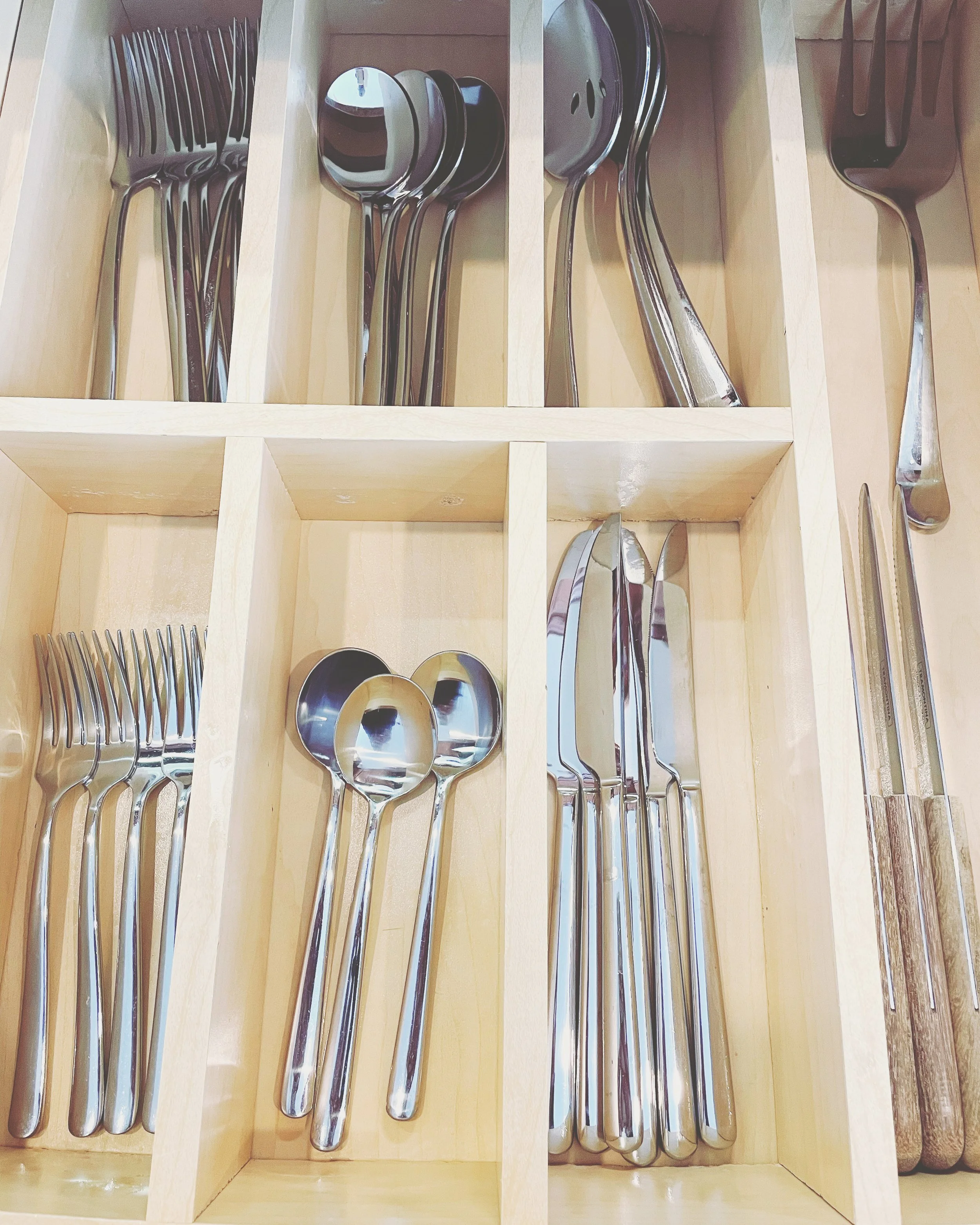 Organized wooden cutlery drawer with sections containing forks, spoons, knives, and various kitchen utensils.