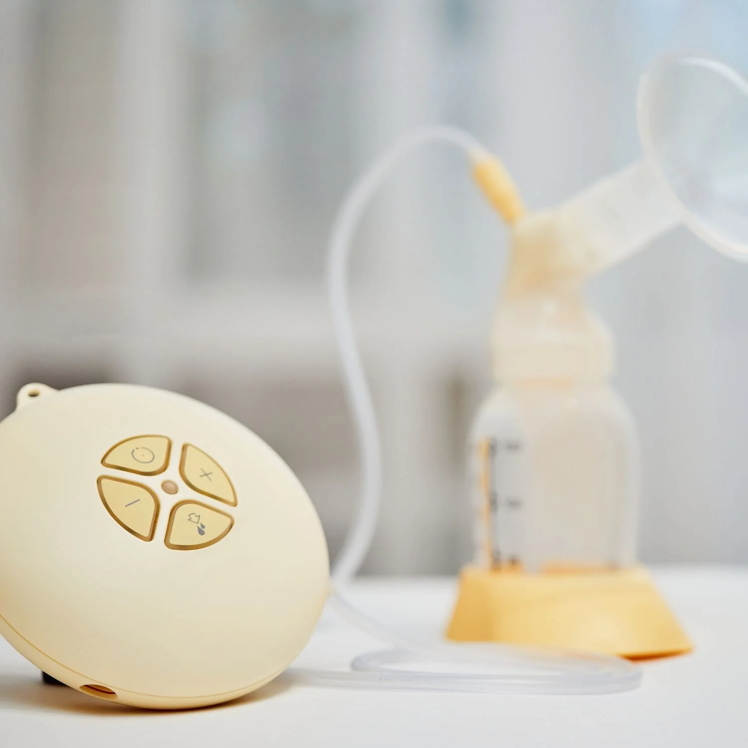 A yellow breast pump with control buttons connected to a clear silicone breast shield and tubing.