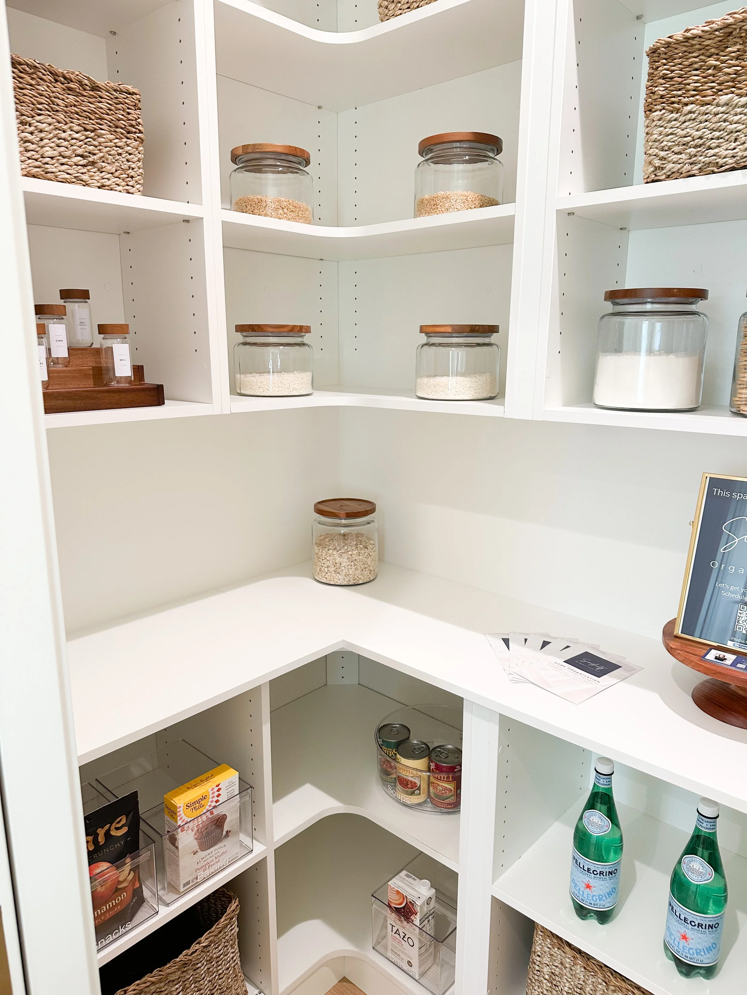 Empty organized pantry with glass jars, canned goods, bottles of sparkling water, and woven baskets.