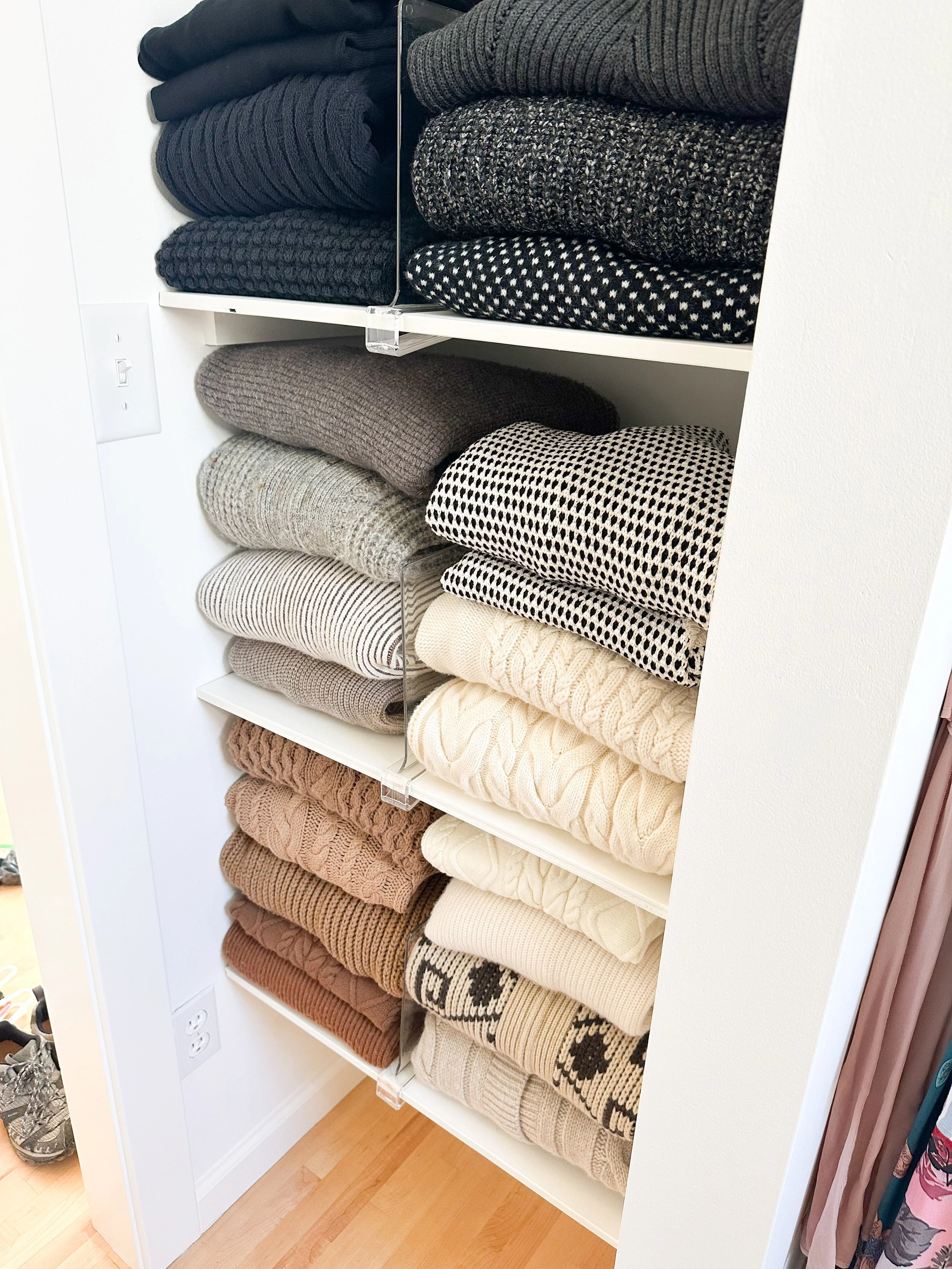 Shelves with various folded sweaters in neutral and dark colors, arranged by color and pattern.