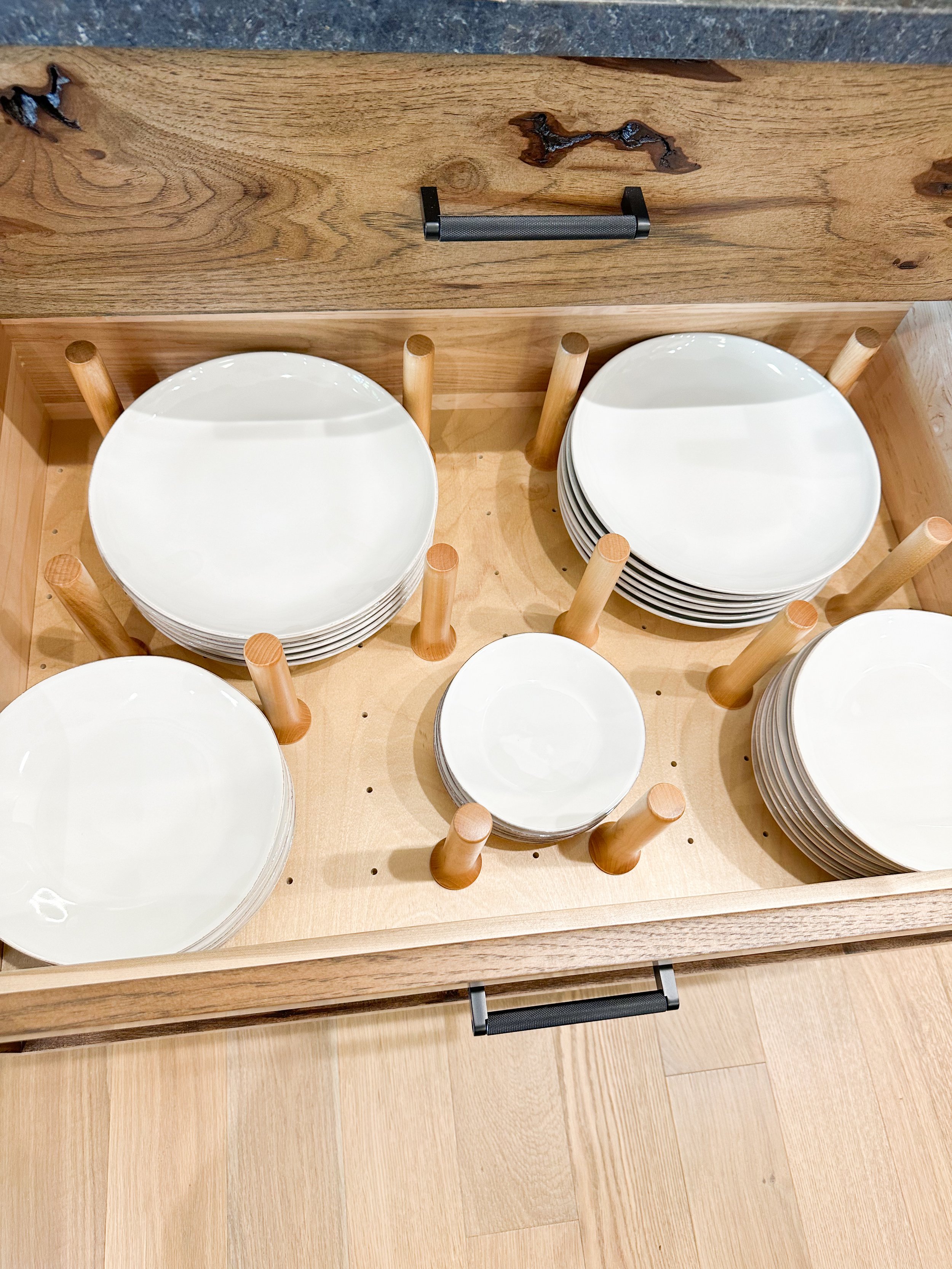 Stack of white plates stored in a wooden drawer with wooden pegs to hold the plates.