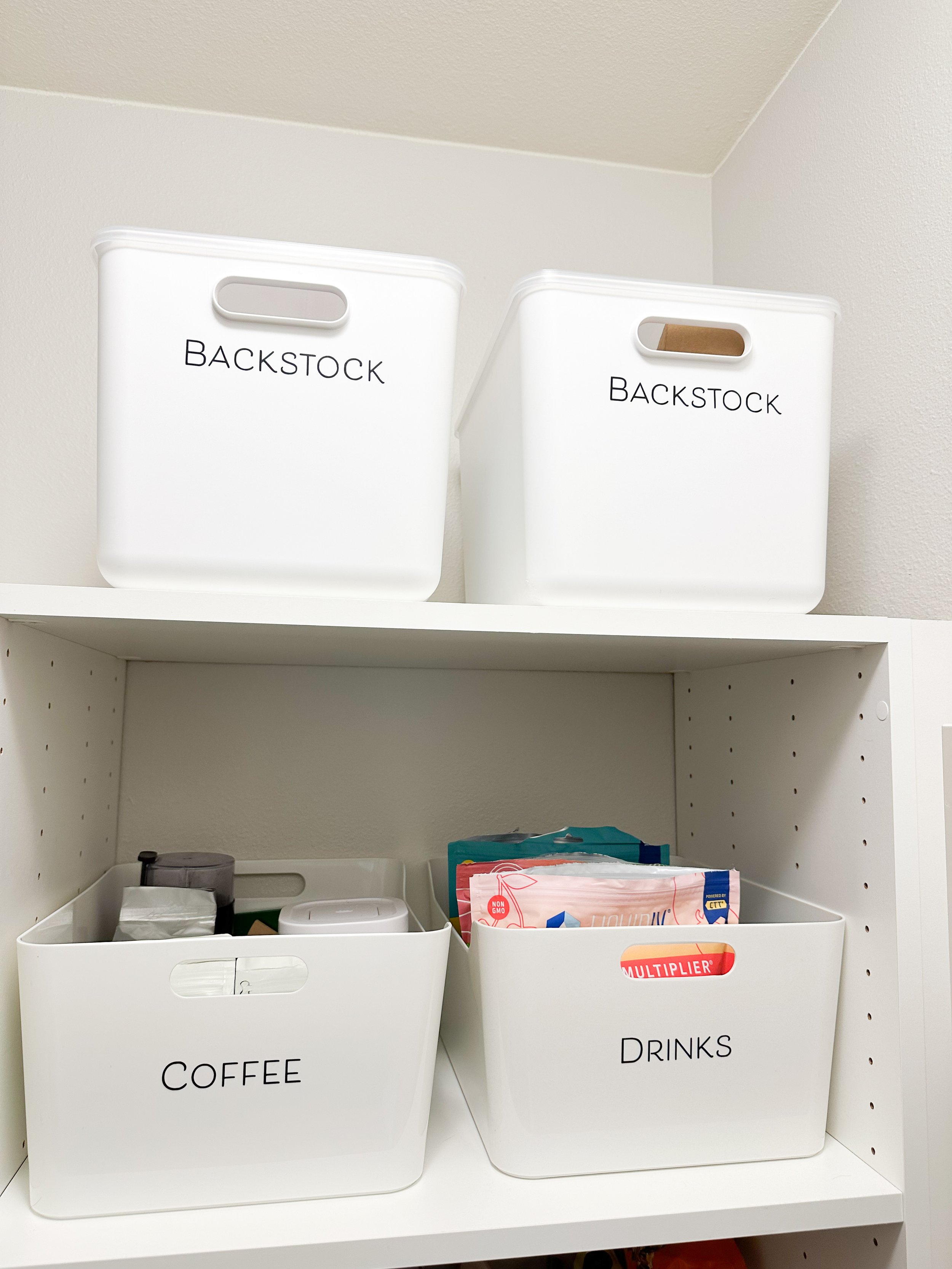 White storage bins labeled 'Backstock' on top shelf, and bins labeled 'Coffee' and 'Drinks' on lower shelf, with various contents inside.