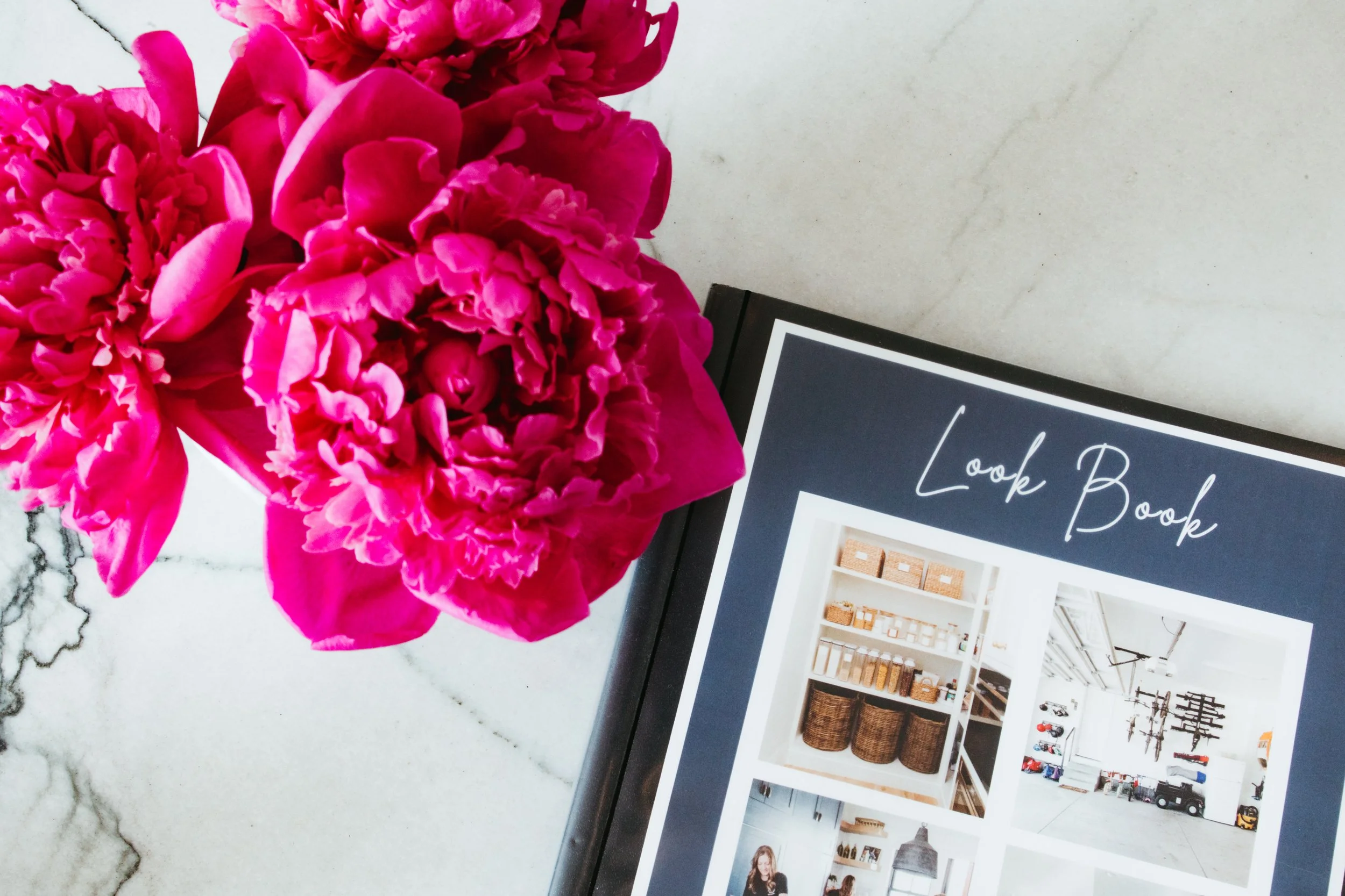 Pink flowers next to a design book titled 'Look Book' on a white marble surface.