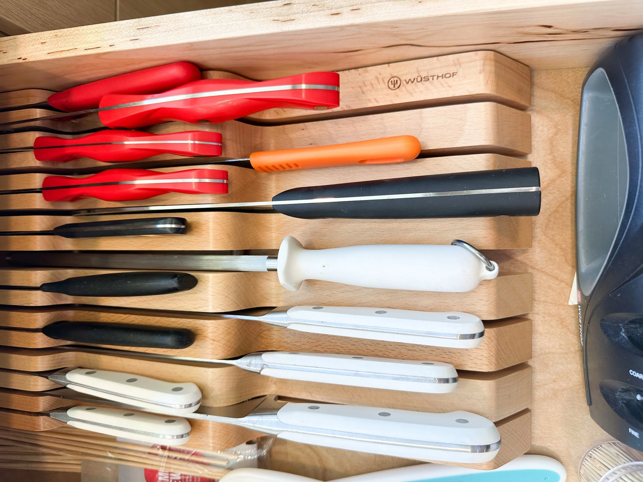 A knife block holding various kitchen knives with handles in colors like red, black, orange, and white, placed on a wooden surface.