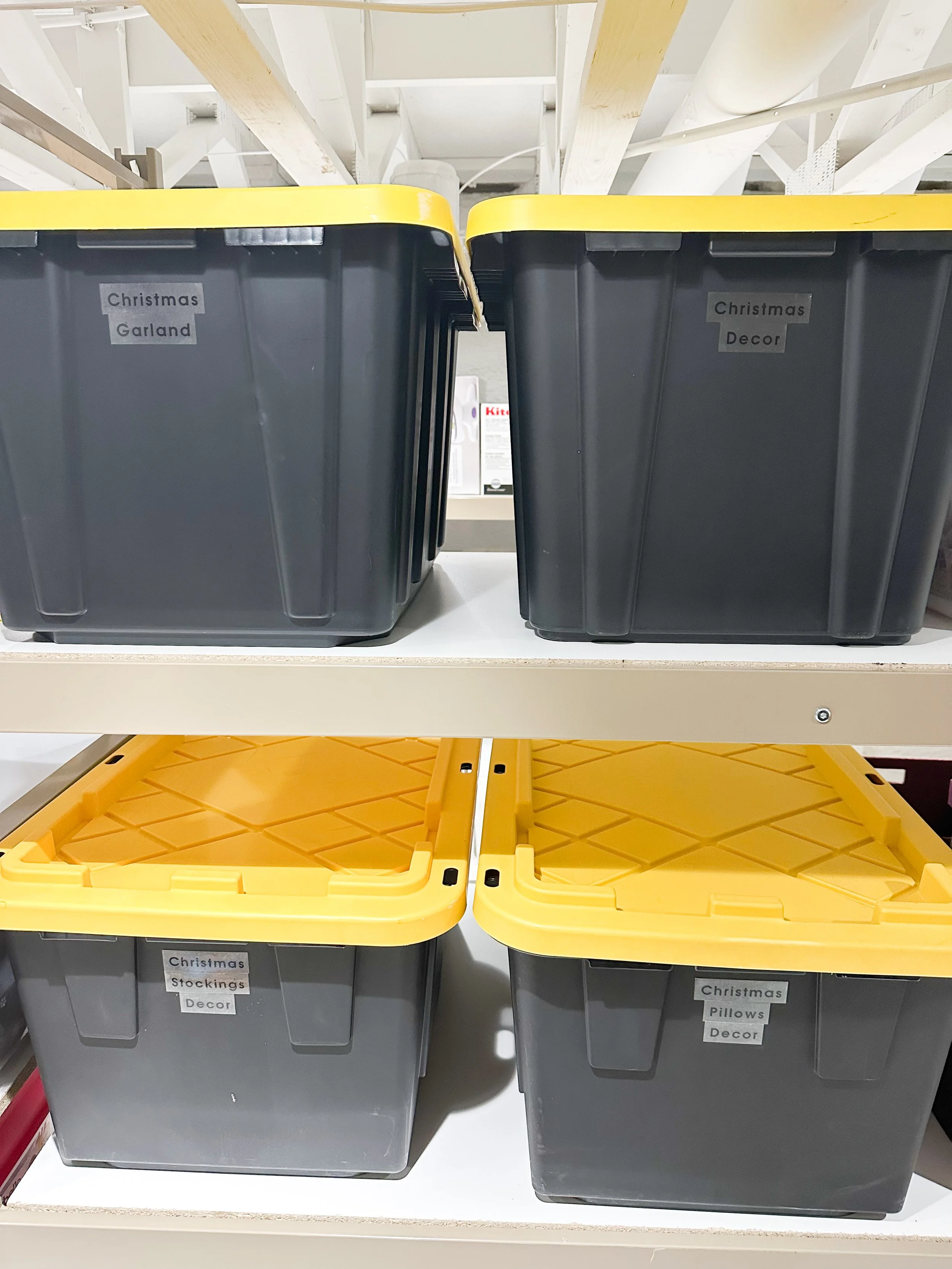 Shelves with black and yellow storage bins labeled 'Christmas Garland,' 'Christmas Decor,' 'Christmas Stockings Decor,' and 'Christmas Pillows Decor' in a store.