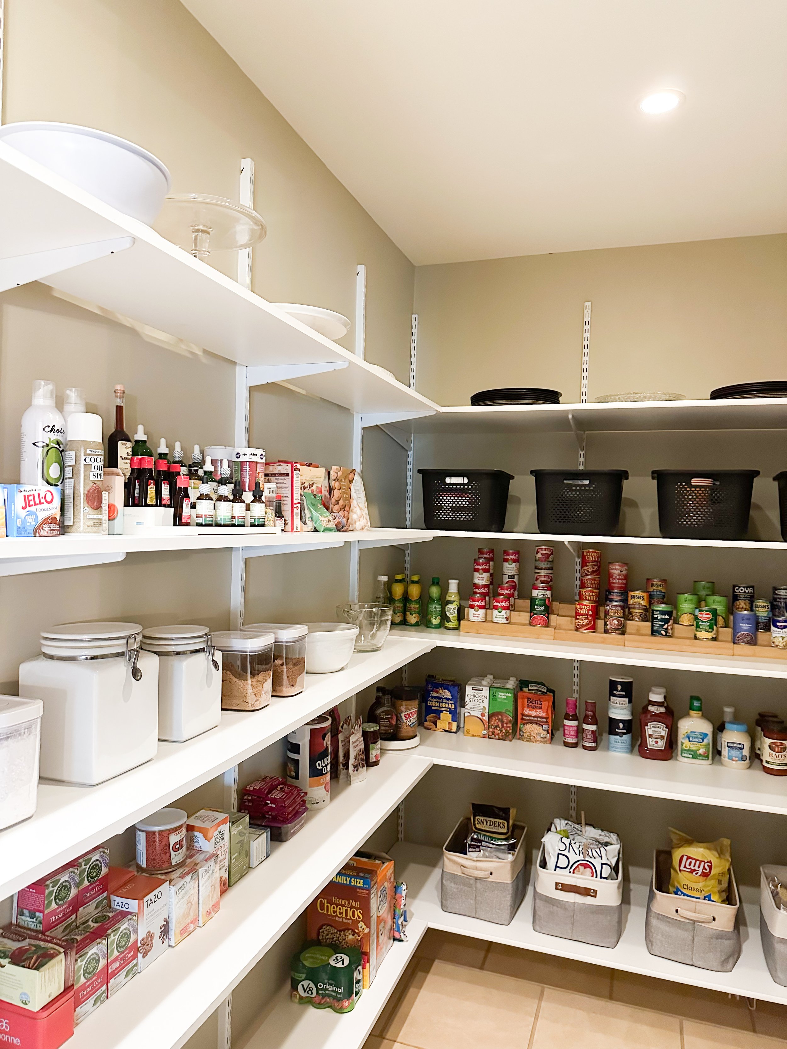 Pantry with white shelves stocked with various food and baking items, including canned goods, bottles, boxes, and containers.