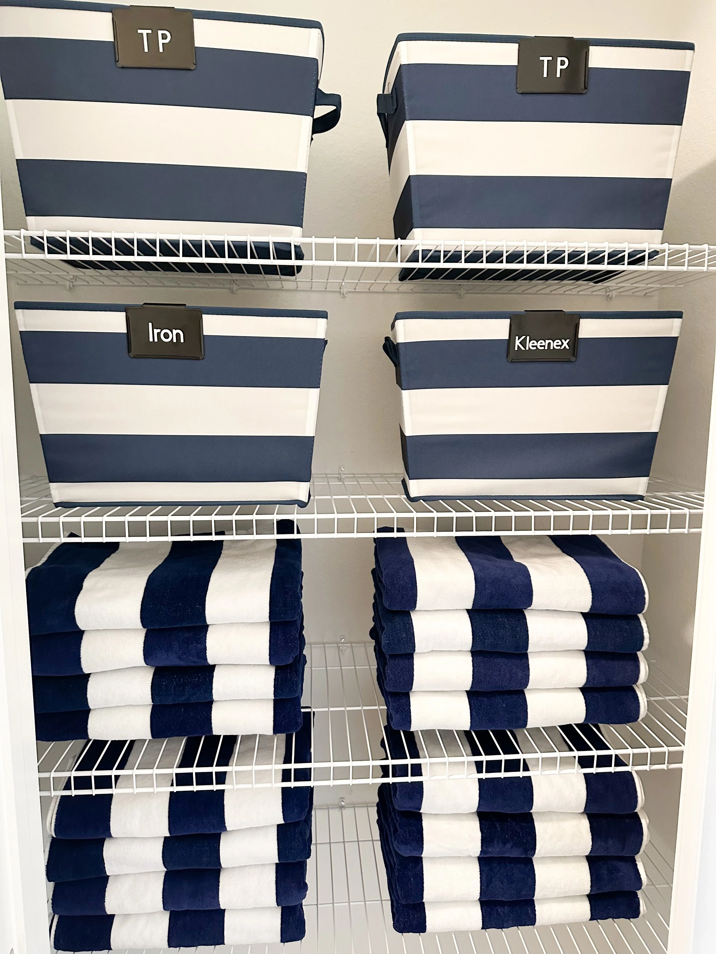 Shelf with striped storage bins labeled TP, TP, Iron, and Kleenex, and matching folded towels with blue and white stripes.