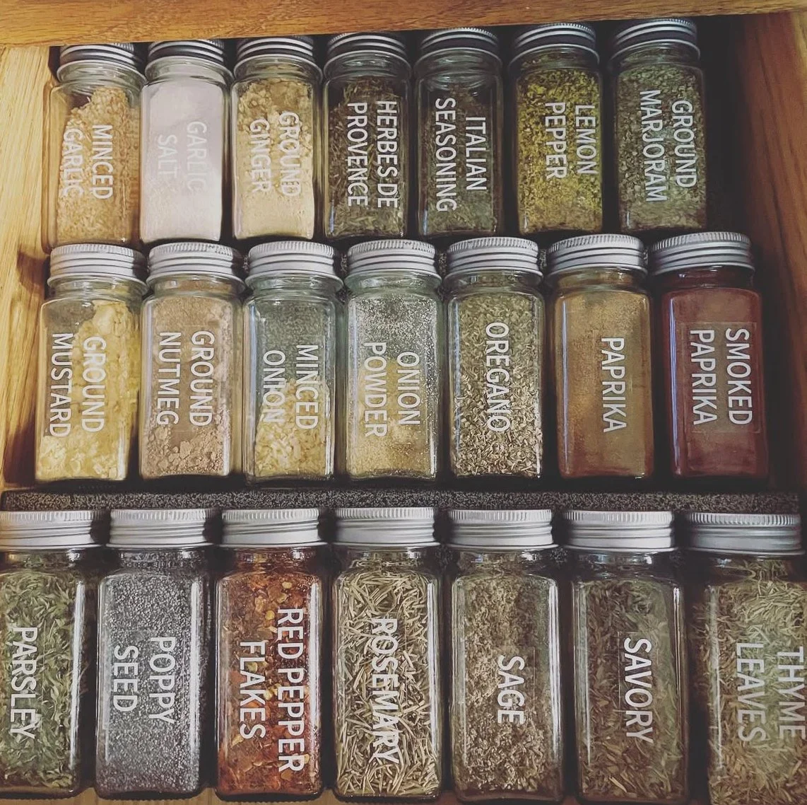Organized spice jars with labels including garlic salt, ground ginger, herbs de Provence, Italian seasoning, lemon pepper, ground wasabi, mustard, ground nutmeg, minced onion, onion powder, oregano, paprika, smoked paprika, parsley, spicy seed, red pepper flakes, rosemary, sage, thyme, and leaves.
