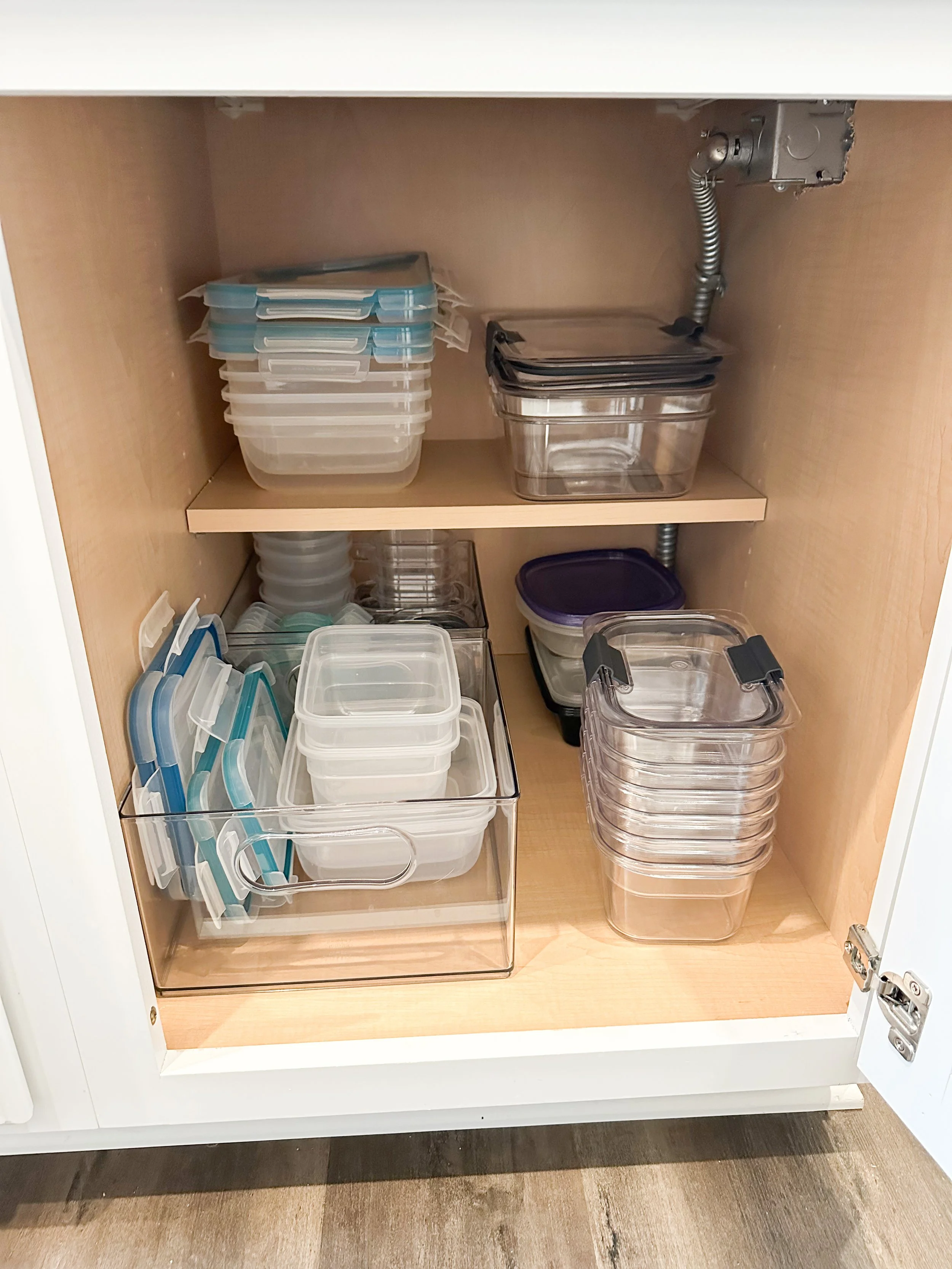 Kitchen cabinet filled with plastic storage containers and lids, organized on shelves.