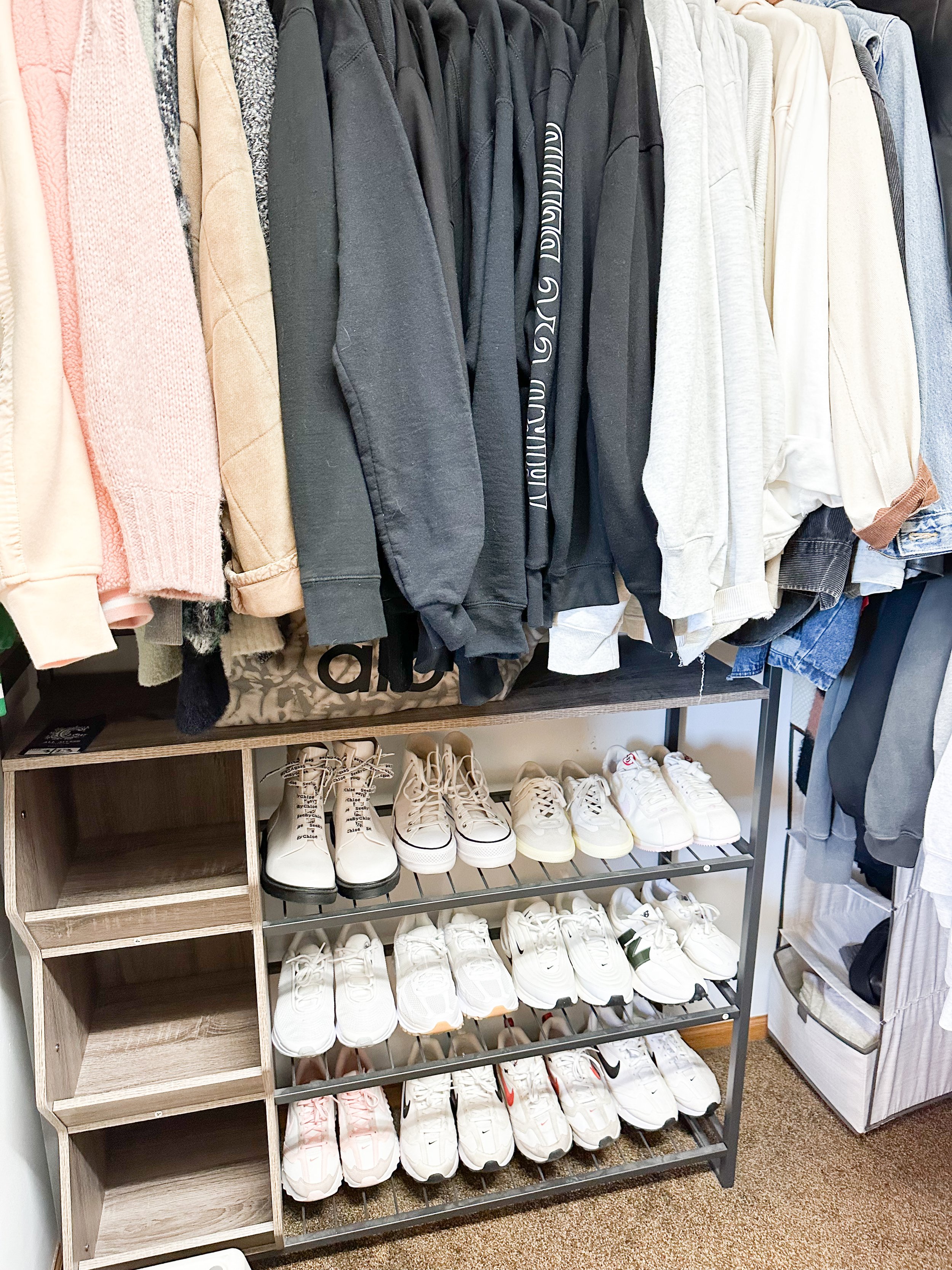 Clothing rack with hoodies and sweatshirts above a shoe shelf with various white sneakers, some with red or black accents, in a store.