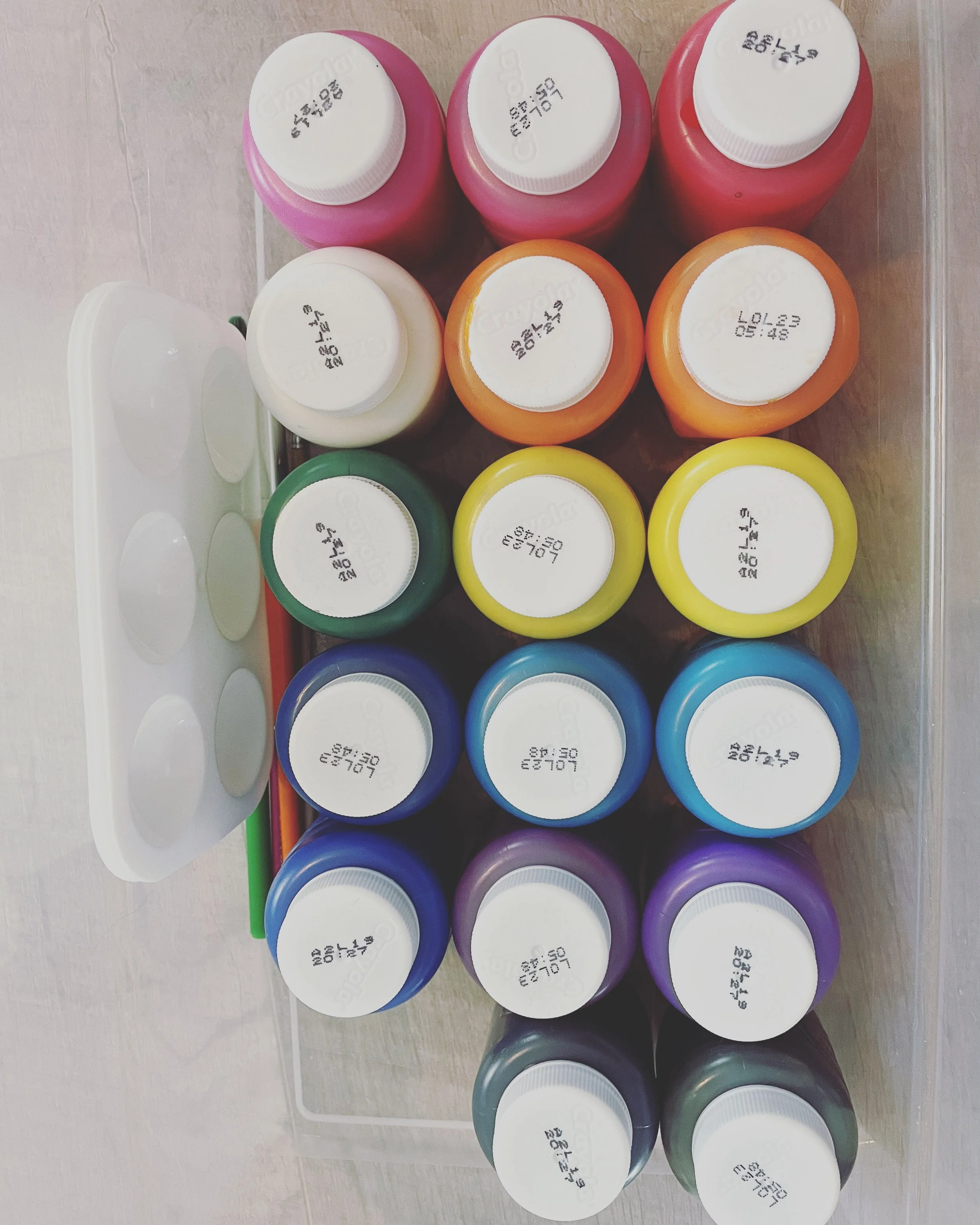 Colorful bottles of paint or craft supplies arranged on a surface, viewed from the top.