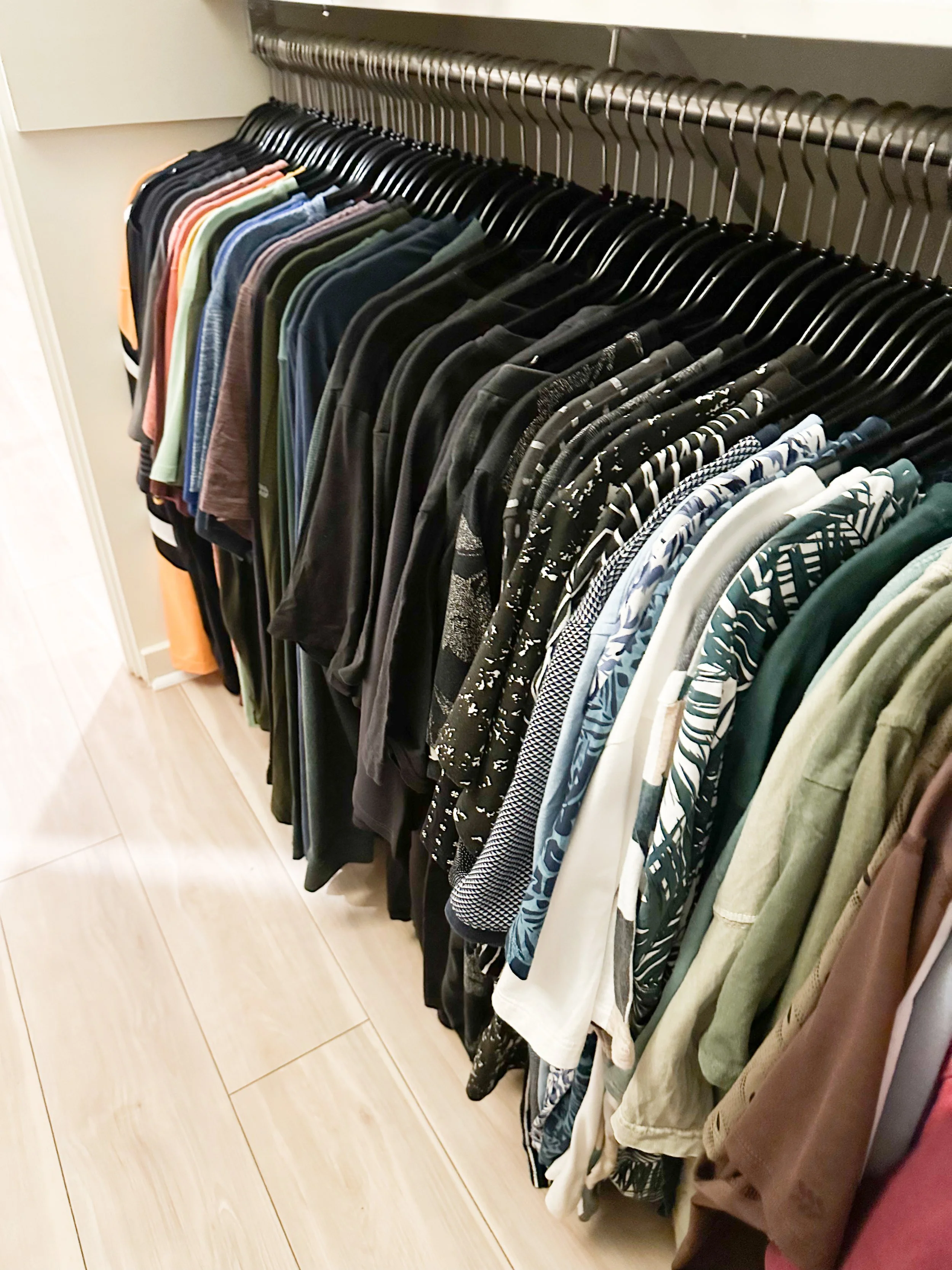 A closet shelf holding a row of hanging T-shirts in various colors and patterns.