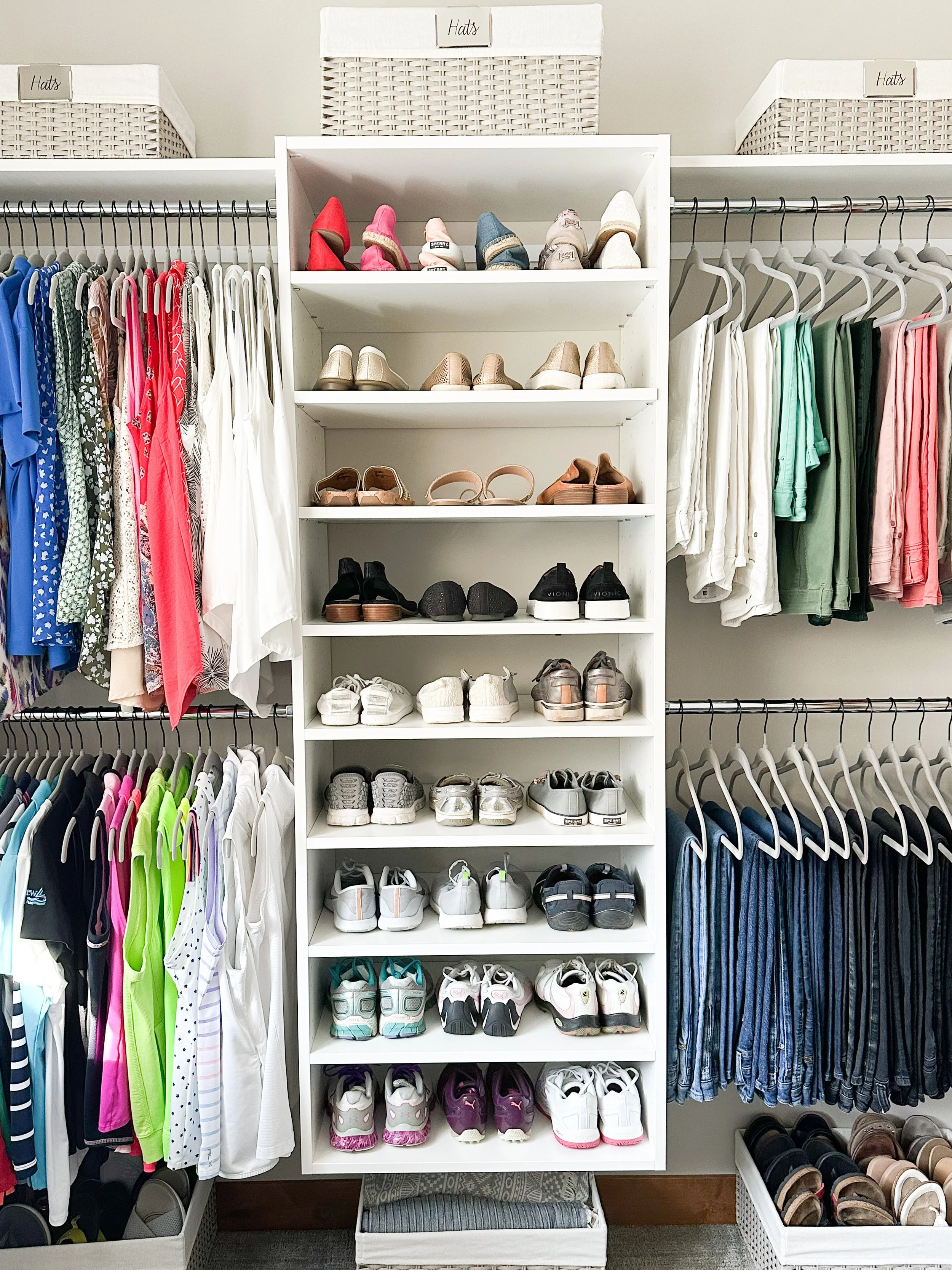 White shelving unit with shoes on shelves and clothing on rods on either side, in a clothing store. Top shelf contains colorful women's shoes, lower shelves have various sneakers and athletic shoes.