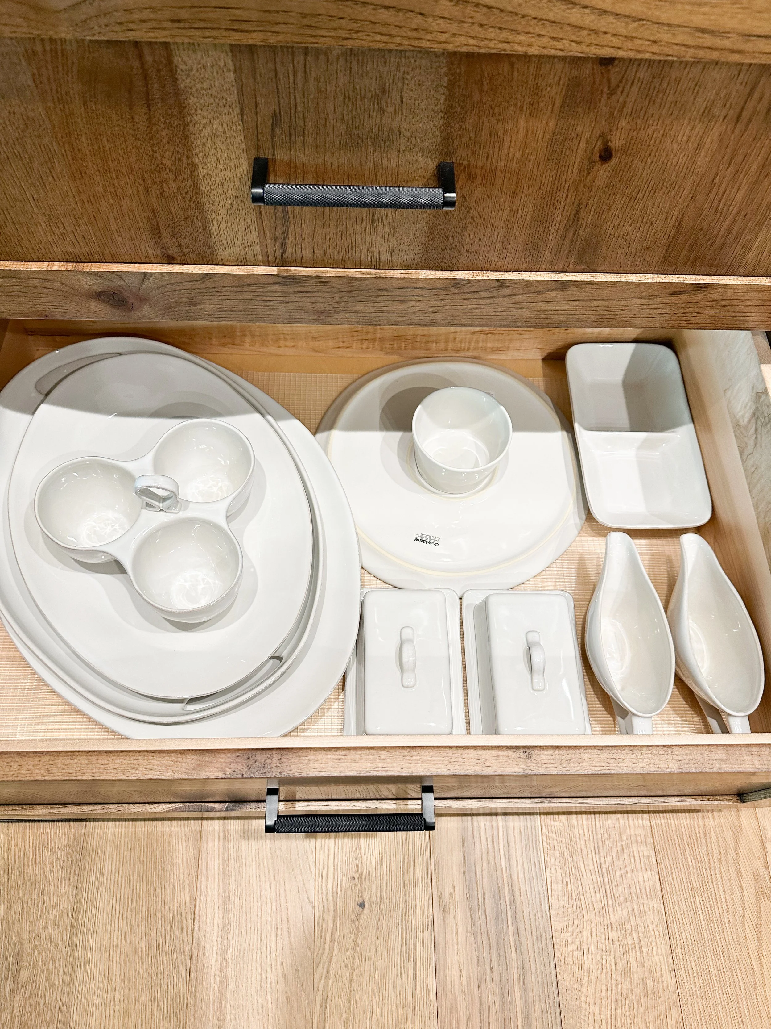Wooden drawer containing assorted white ceramic and porcelain dishware including bowls, plates, and utensil holders.