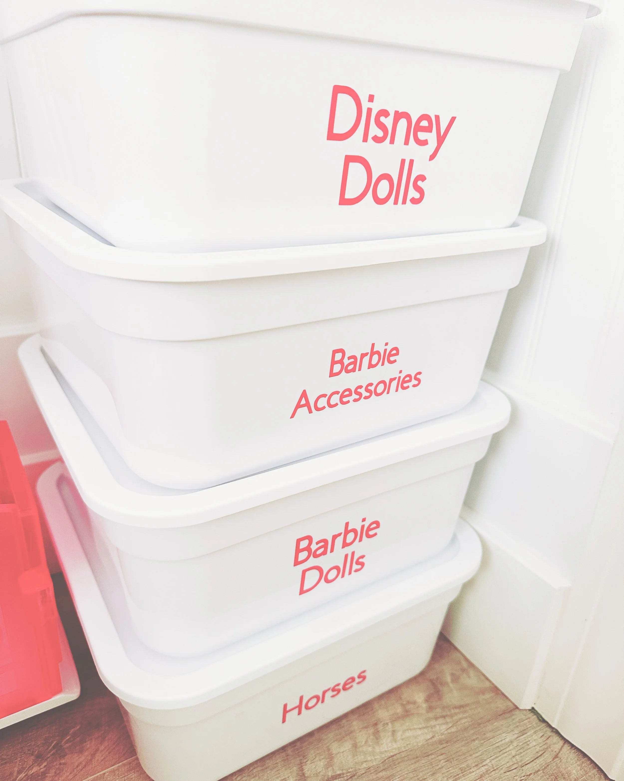Stack of white plastic storage bins labeled "Disney Dolls," "Barbie Accessories," "Barbie Dolls," and "Horses" in pink text.