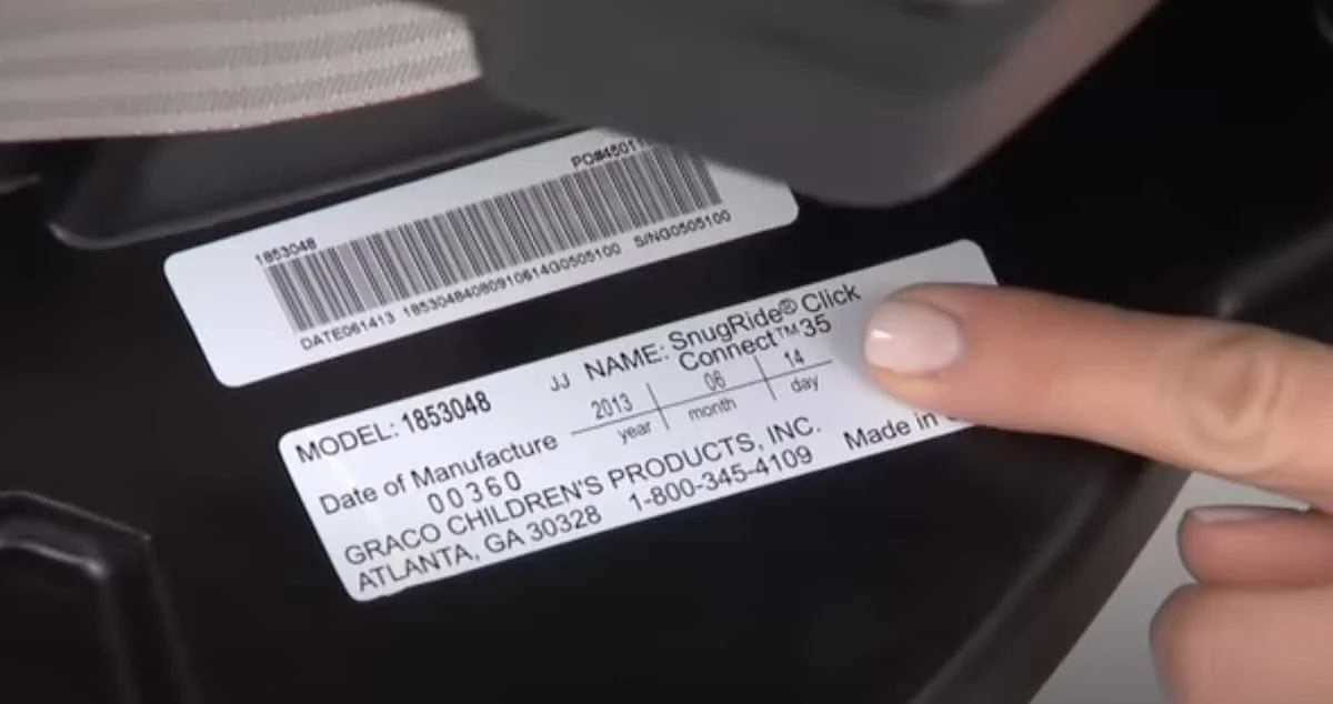 Close-up of a person's finger pointing at a label on a black device, with a barcode and manufacturing information visible.