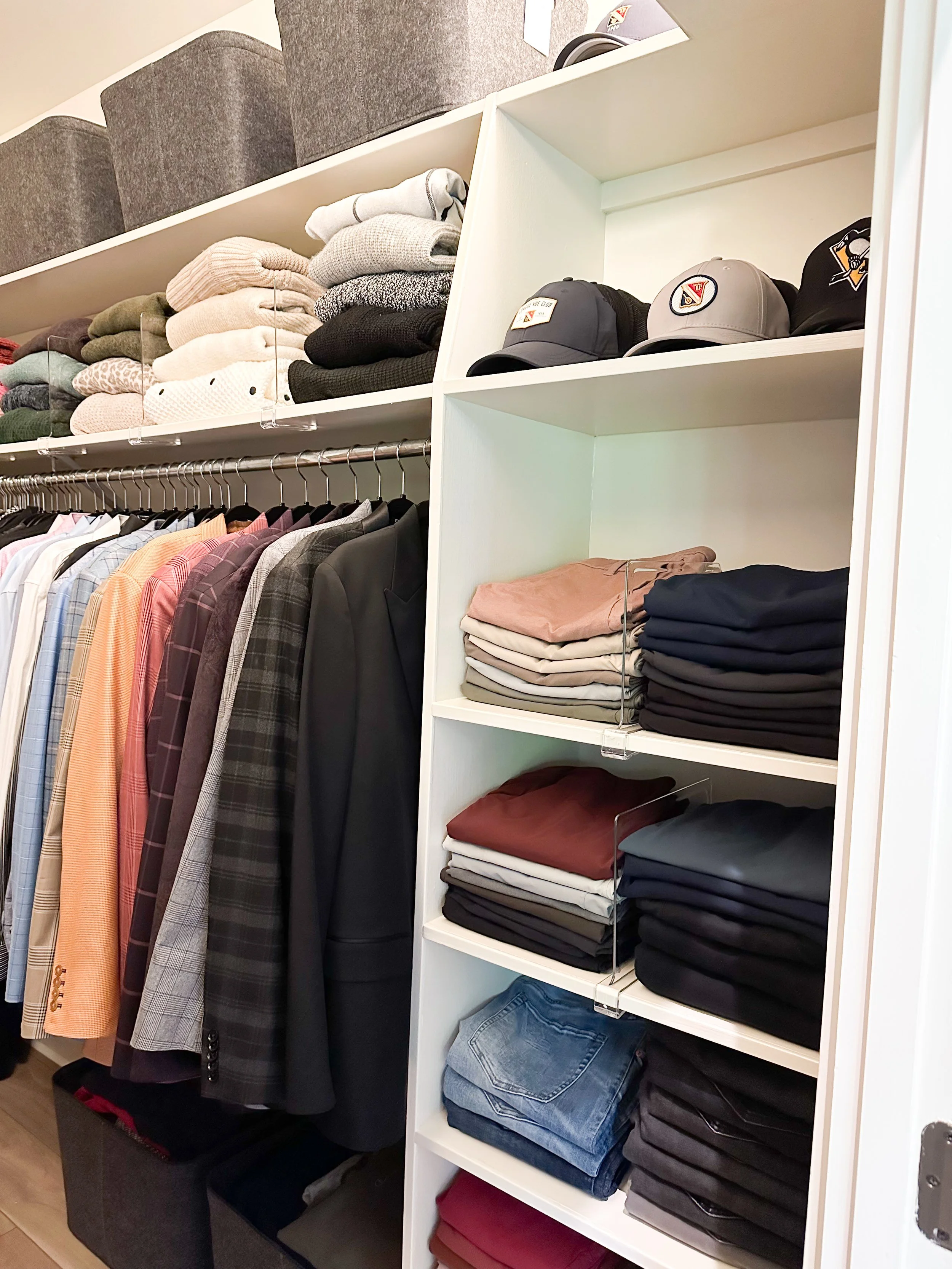 Clothing rack with colorful men's shirts and jackets, and shelves with folded pants, and hats on top shelf.