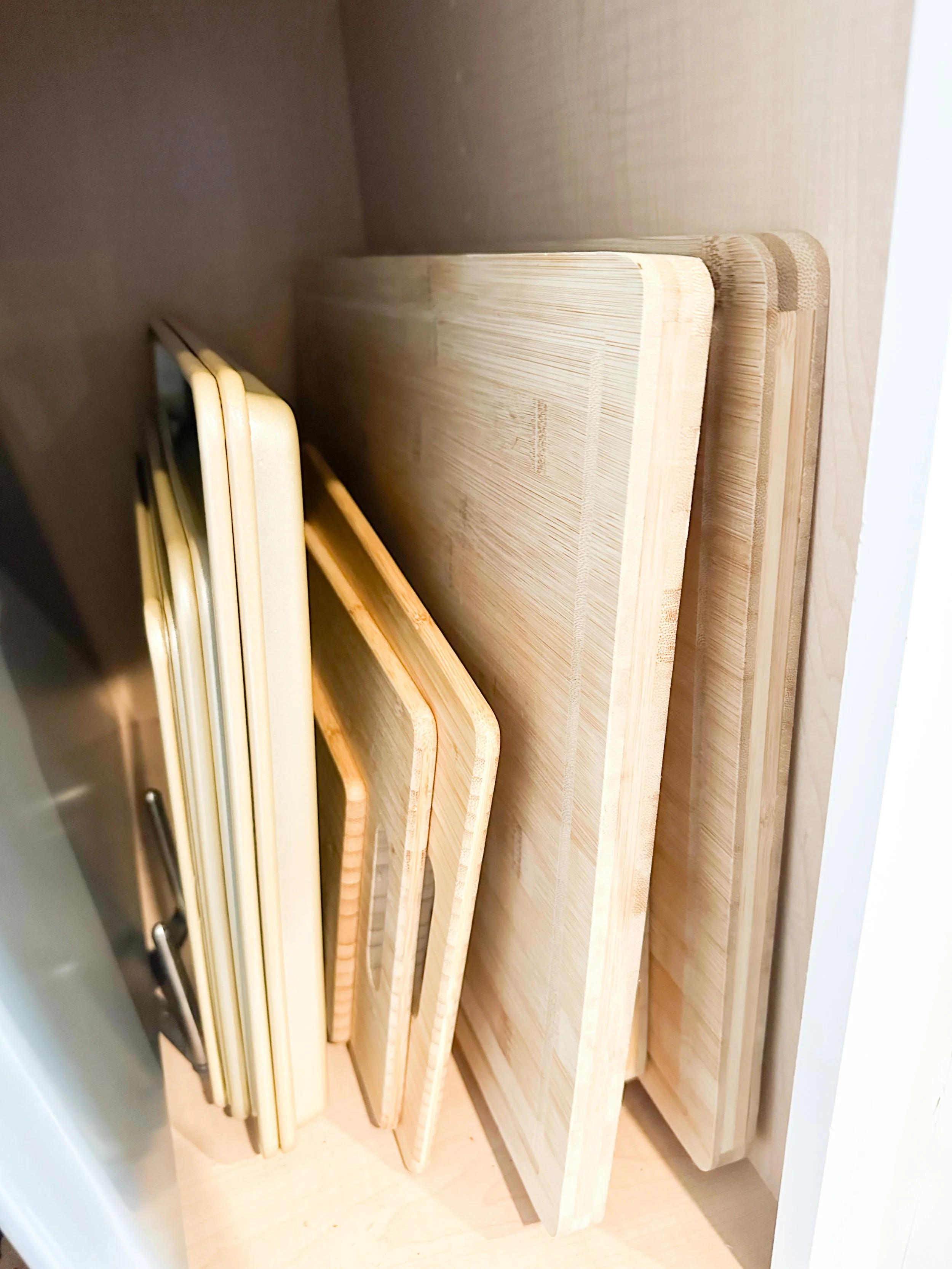 Multiple wooden cutting boards of various sizes and shapes stored upright in a kitchen drawer.