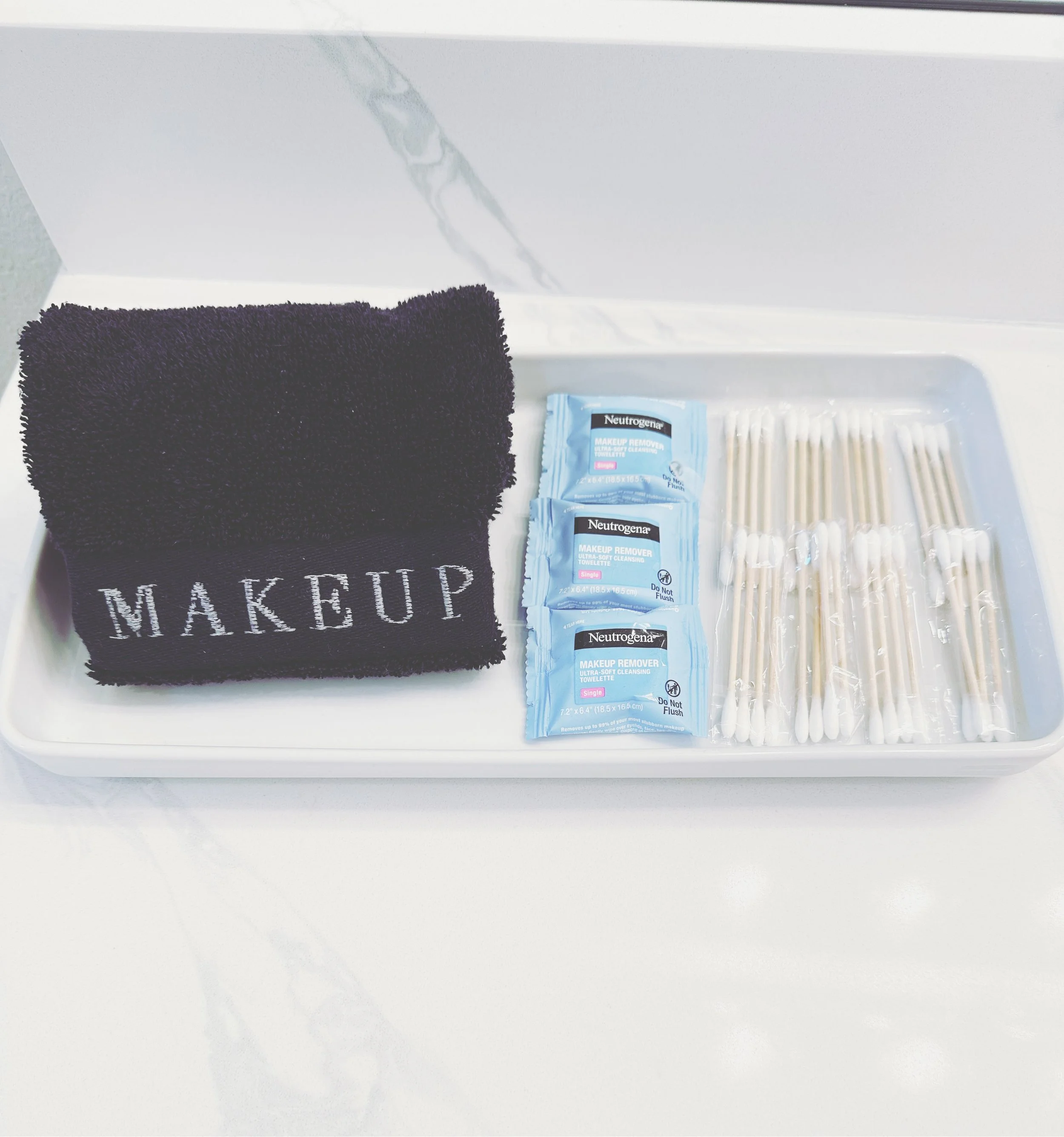 Tray with black cloth labeled 'MAKEUP', three packets of Neutrogena makeup remover wipes, and several cotton swabs.