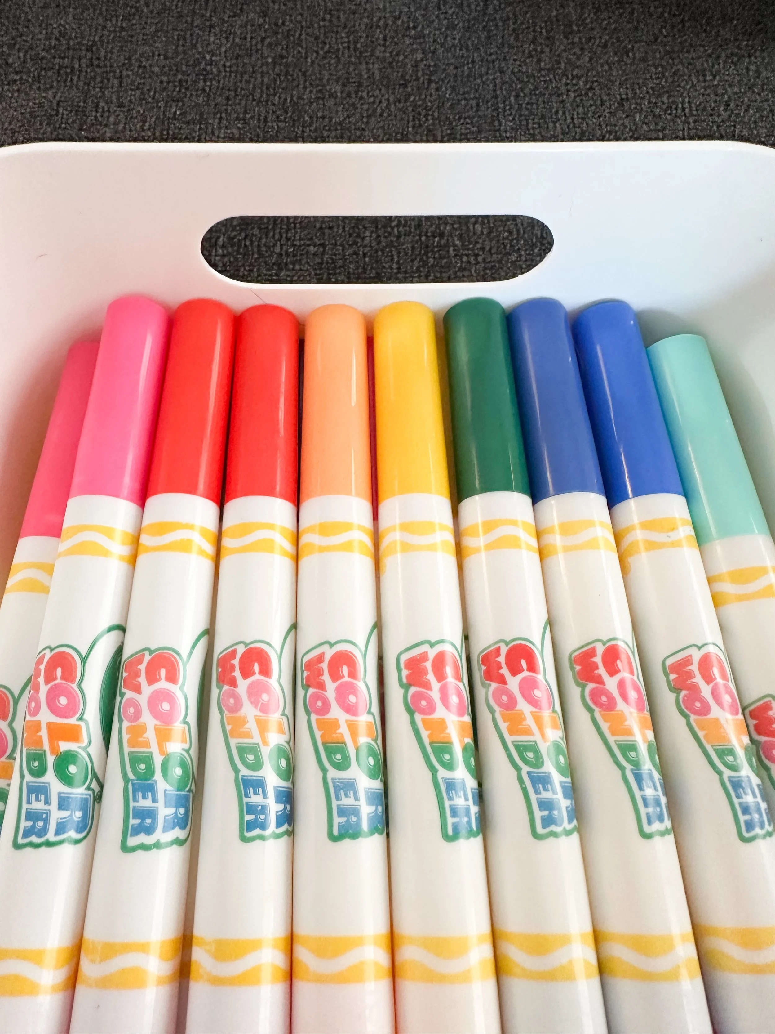 A white plastic tray holding ten colorful markers in shades of pink, red, orange, yellow, green, blue, and light blue.