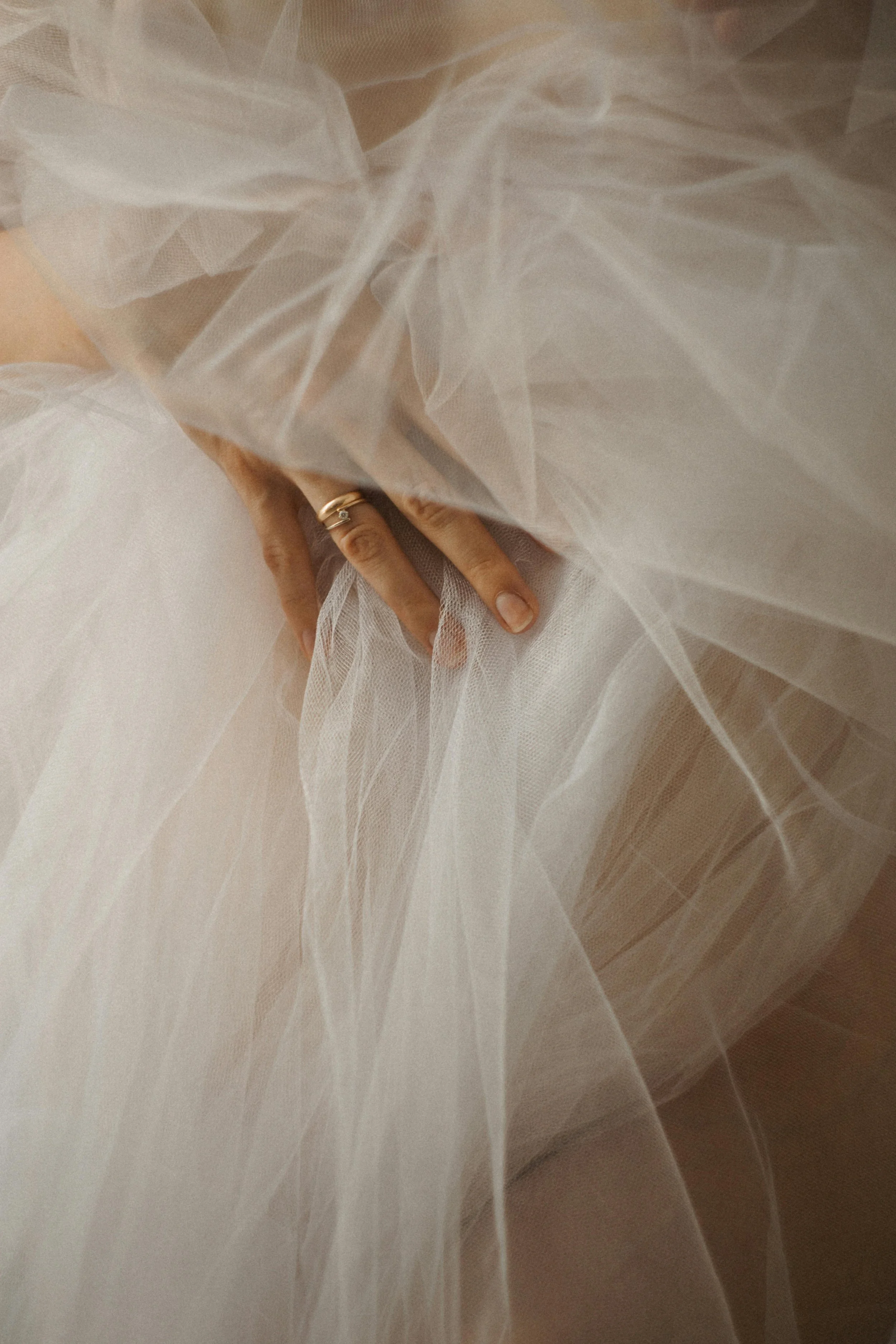 Close-up of a hand gently touching soft, flowing white tulle fabric, wearing a ring.