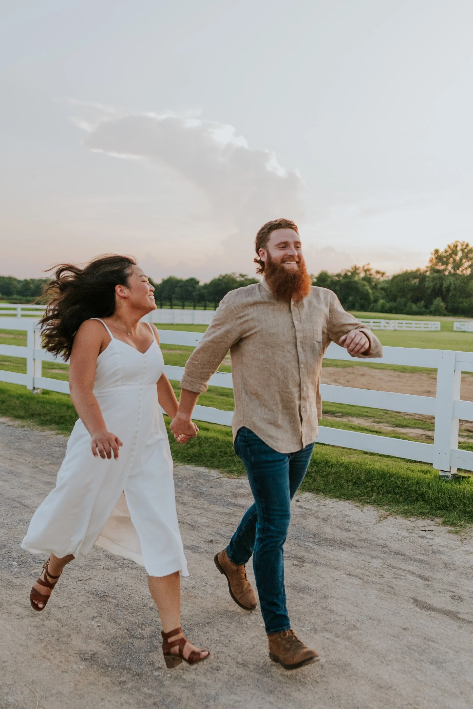 A happy couple holding hands and running outdoors on a farm during sunset.