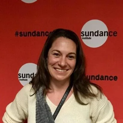 Woman with shoulder-length brown hair smiling in front of a red background with 'sundance' logos.
