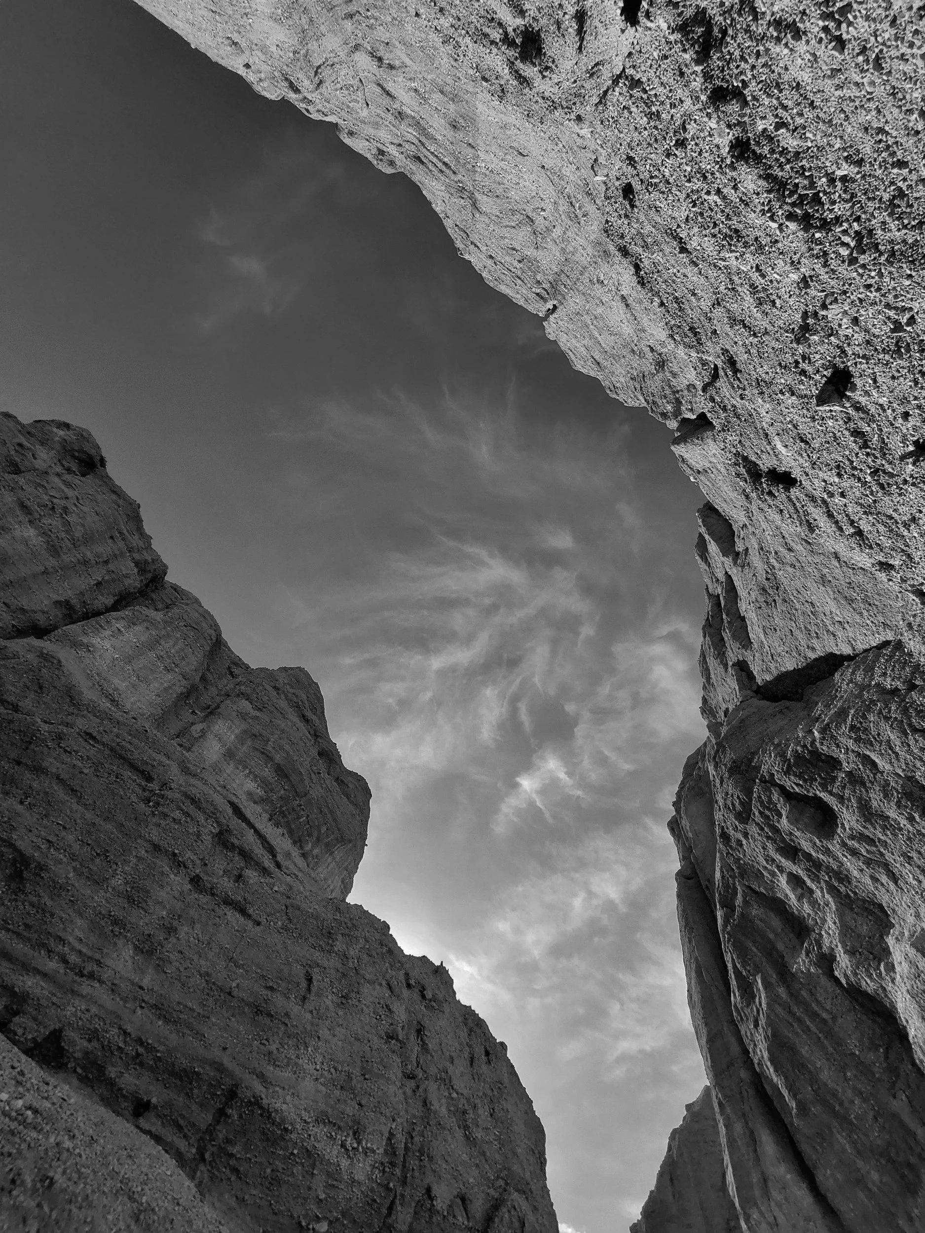 Looking upward between tall, rugged rock formations with a cloudy sky in the background.