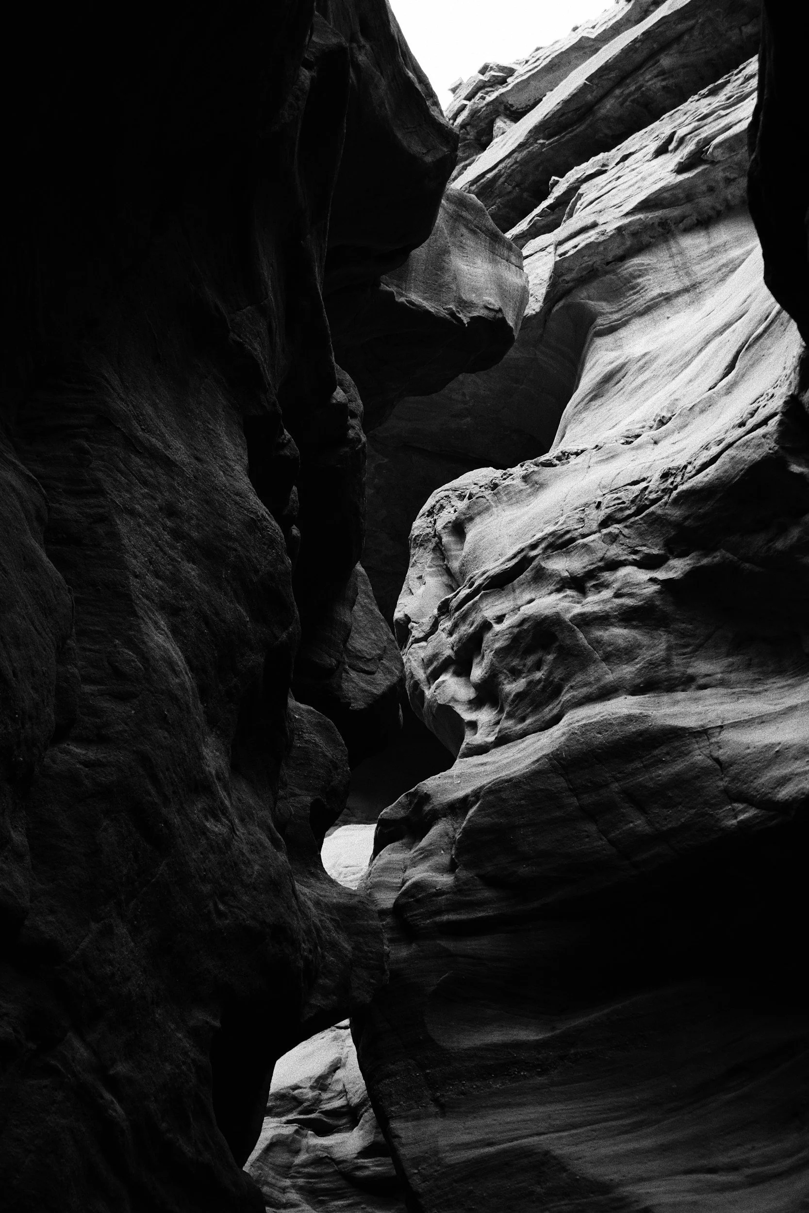 Black and white photo of a narrow slot canyon with smooth, layered rock walls.