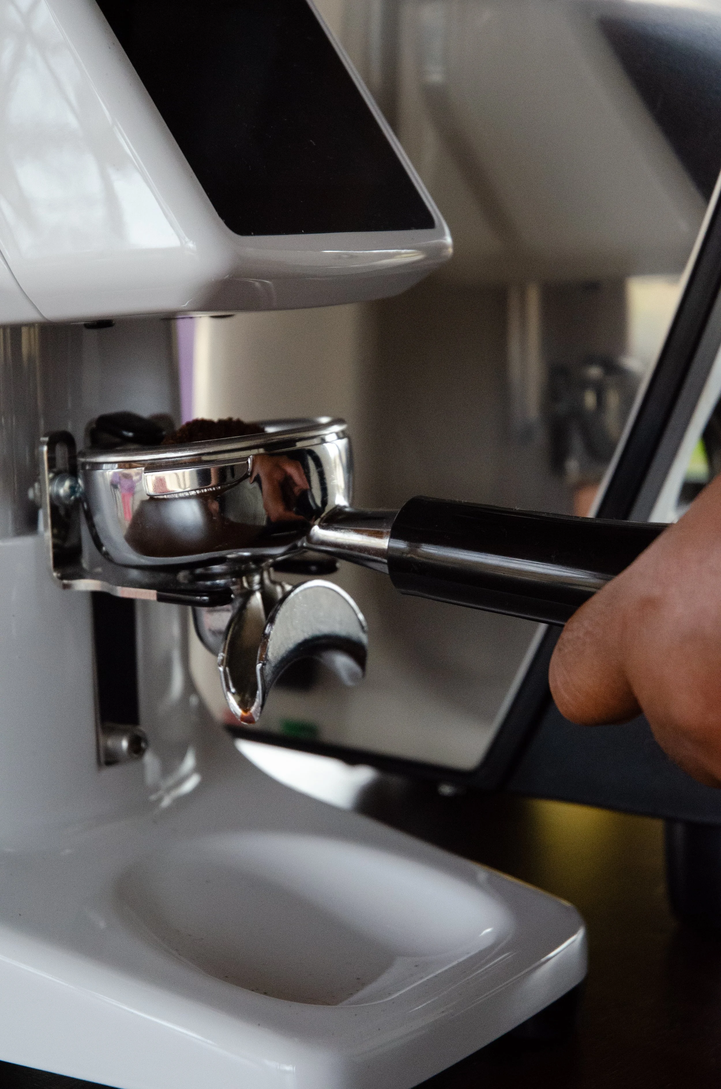 Close-up of a portafilter with coffee grounds being tamped down by a hand, on an espresso machine.