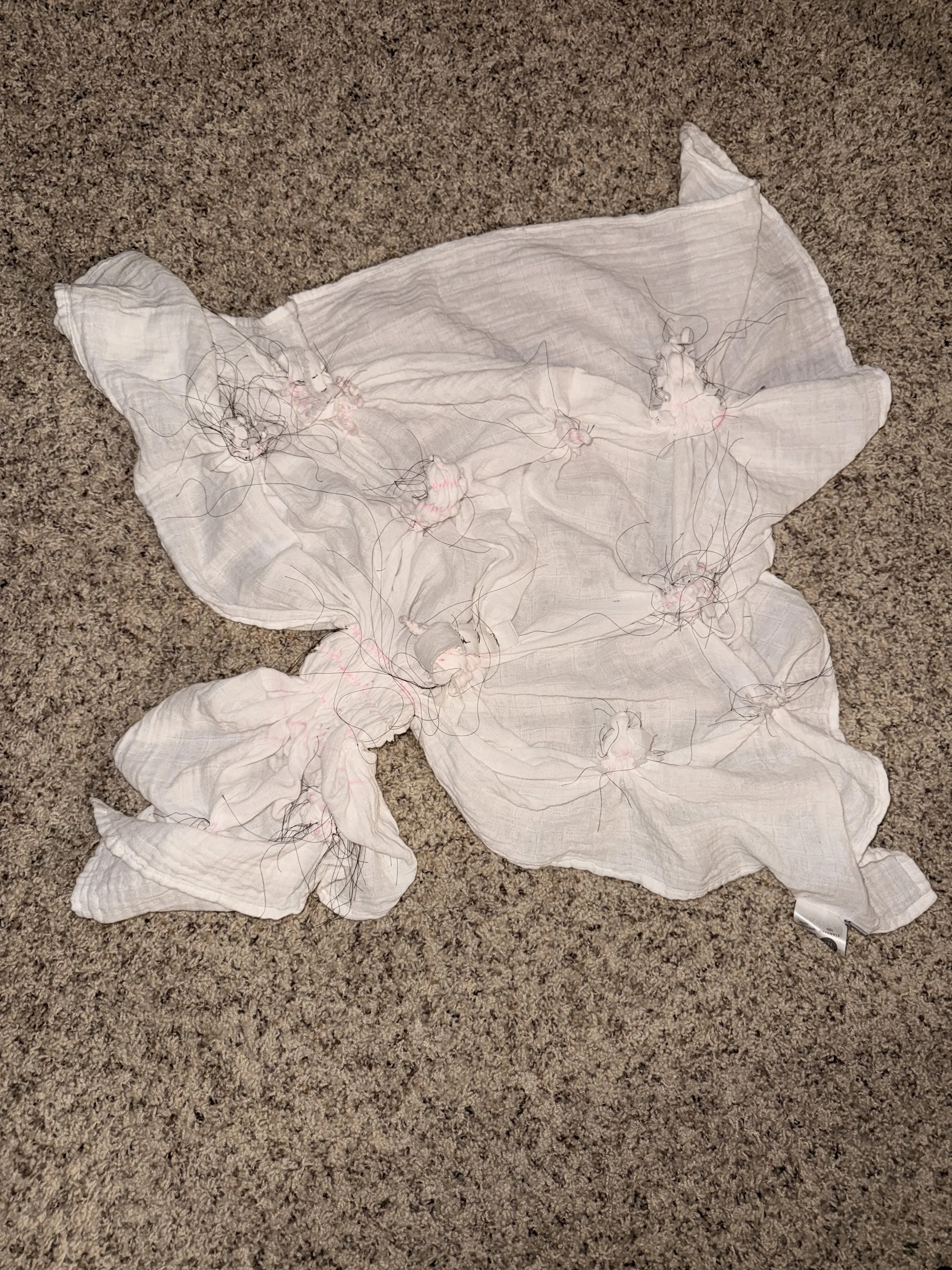 The undyed fabric, with resists added.  Originally a square, the fabric is now distorted due to the tightly-tied threads.